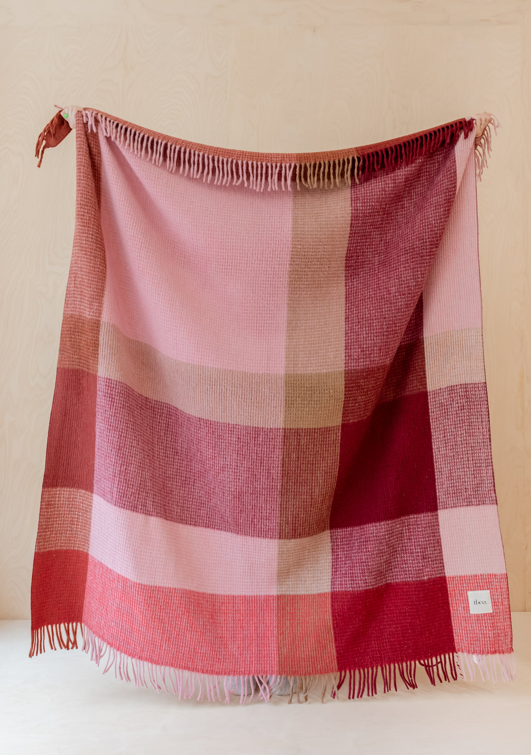 TBCo Recycled Wool Blanket in Berry Waffle Block Check pattern hanging against beige wall, showcasing fringed edges and textured weave