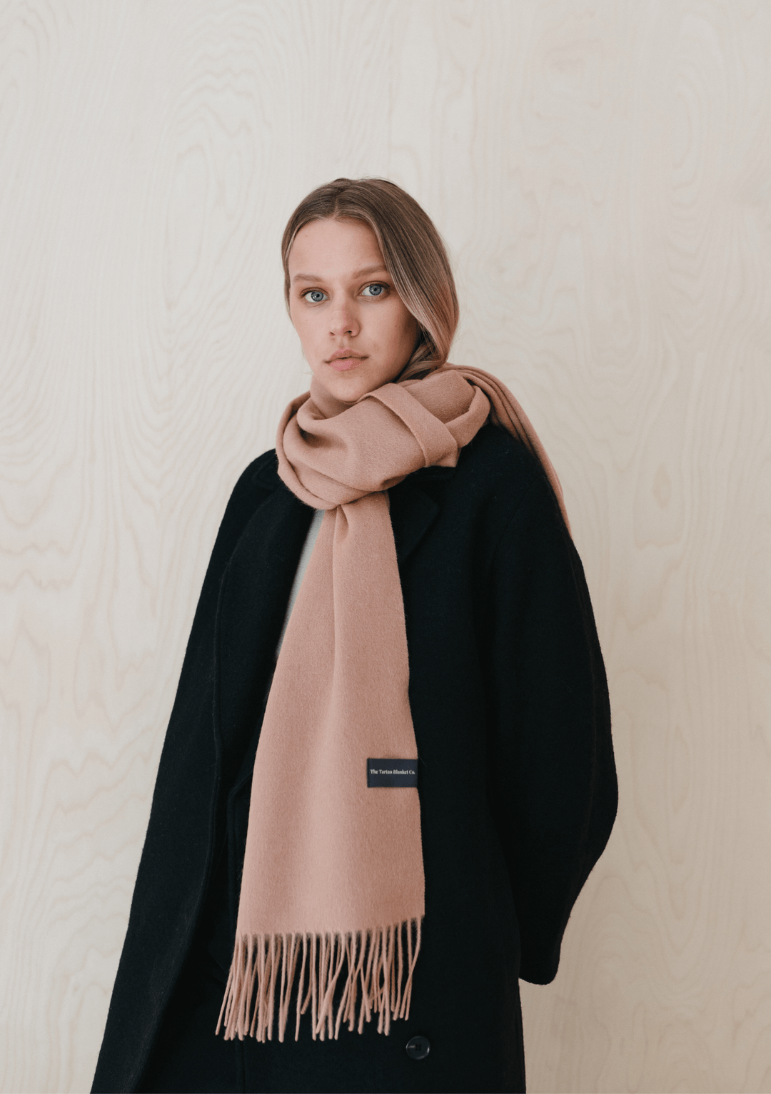 Model wearing TBCo Lambswool Oversized Scarf in Blush draped over black winter coat, showing fringed detail and soft texture