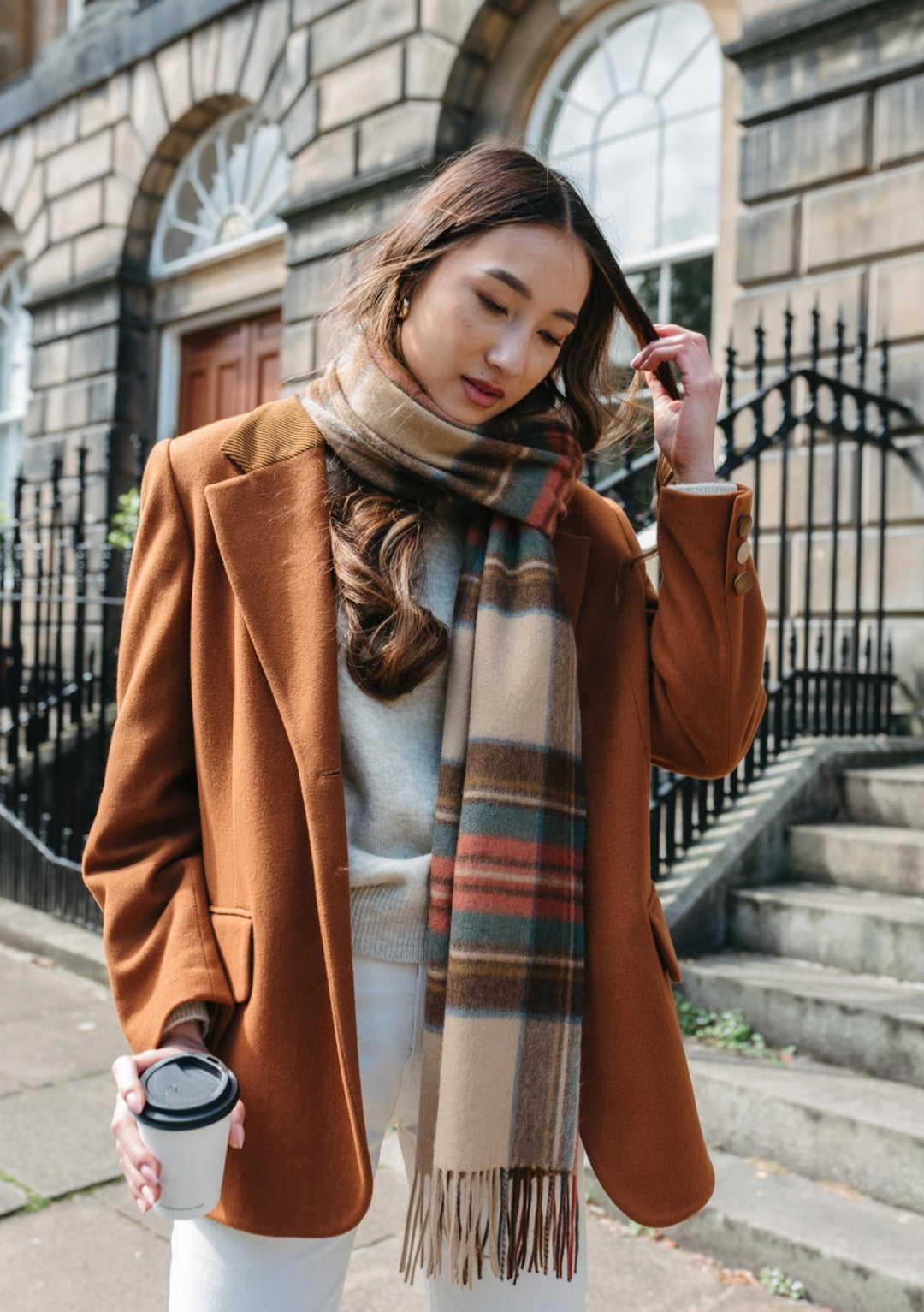 A person wearing TBCo's Stewart Dress Antique Tartan Lambswool Oversized Scarf styled with brown coat on Edinburgh street steps