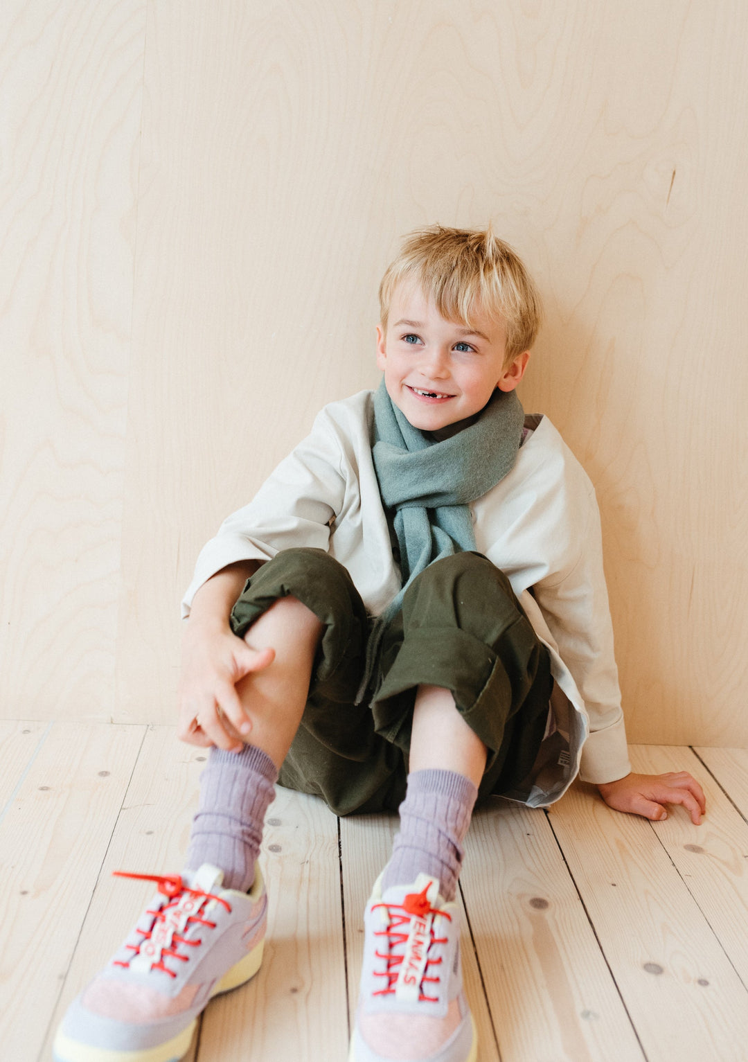 TBCo Lambswool Kids Scarf in Sage Melange shown draped stylishly on wooden floor with cosy winter styling