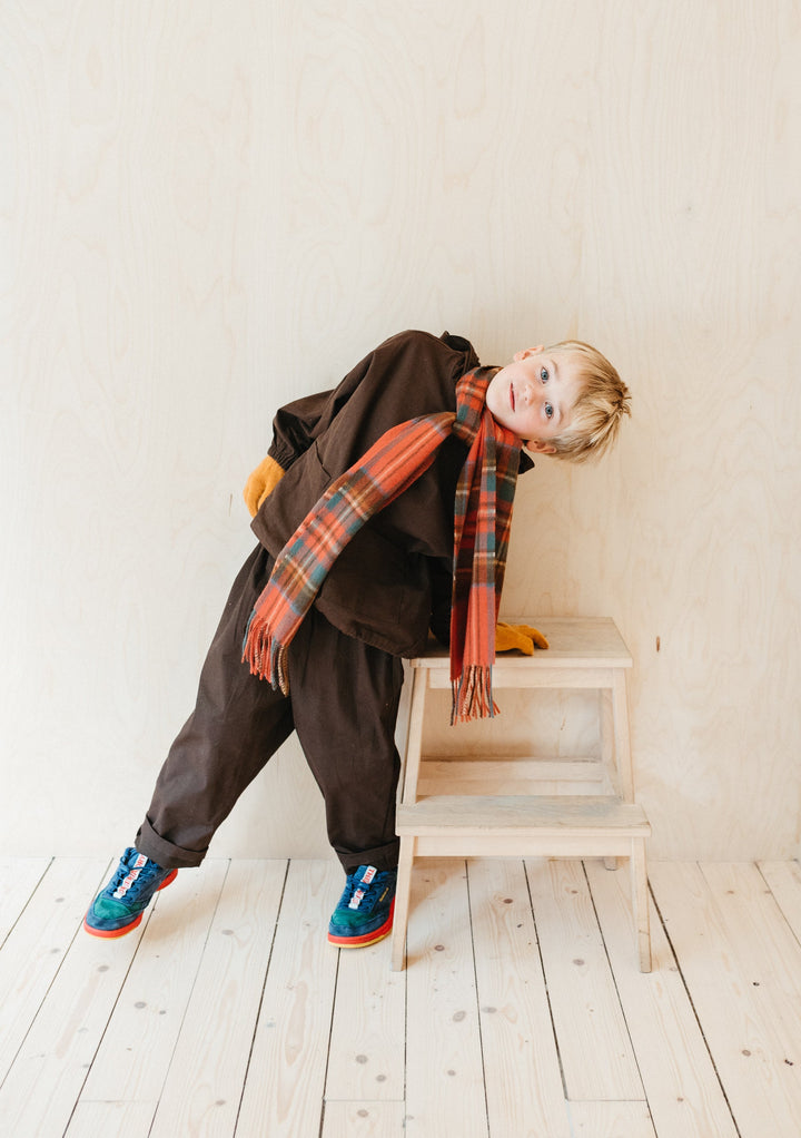 Young child wearing TBCo Lambswool Kids Scarf in Stewart Royal Antique Tartan with brown outfit on wooden steps