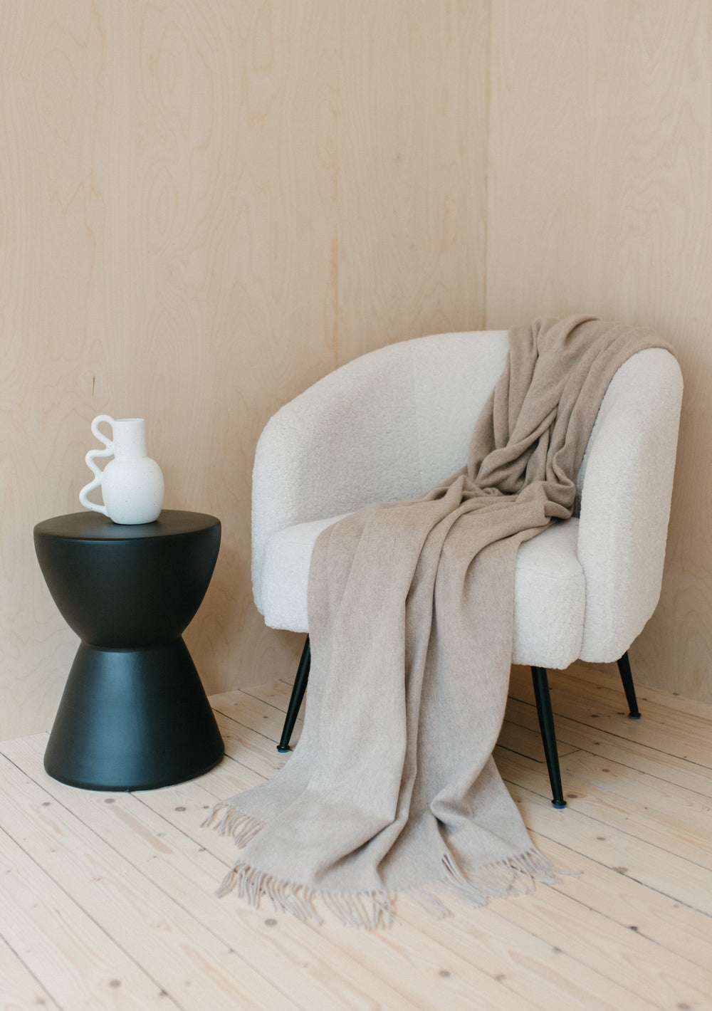 TBCo Lambswool Blanket in Oatmeal Melange draped over white accent chair with black stool and decorative white vase