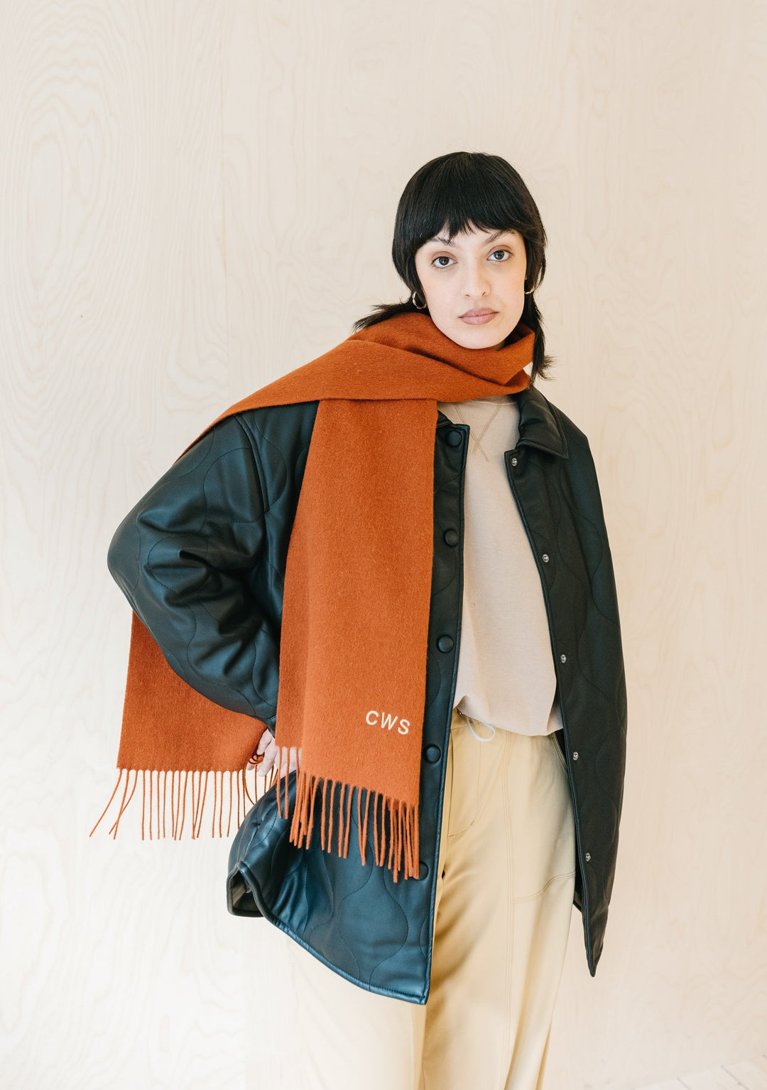 Rust melange TBCo lambswool scarf with fringe styled on model with dark jacket and cream trousers against neutral backdrop