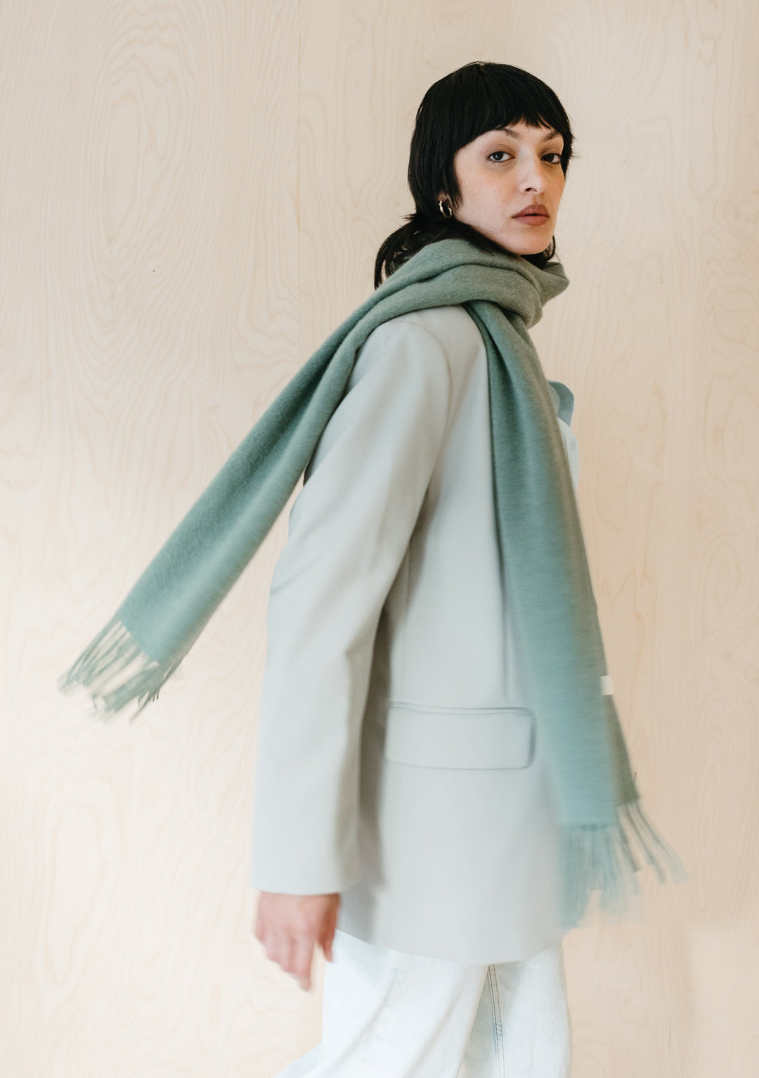 TBCo Lambswool Scarf in Sage Melange draped elegantly over white winter coat, showcasing soft texture and fringed edges