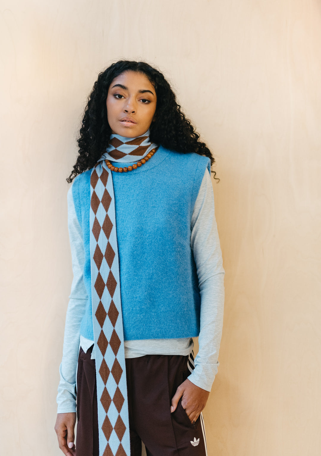 Model wearing TBCo Merino Wool Skinny Scarf in Brown Harlequin with blue and brown diamond pattern wrapped around neck