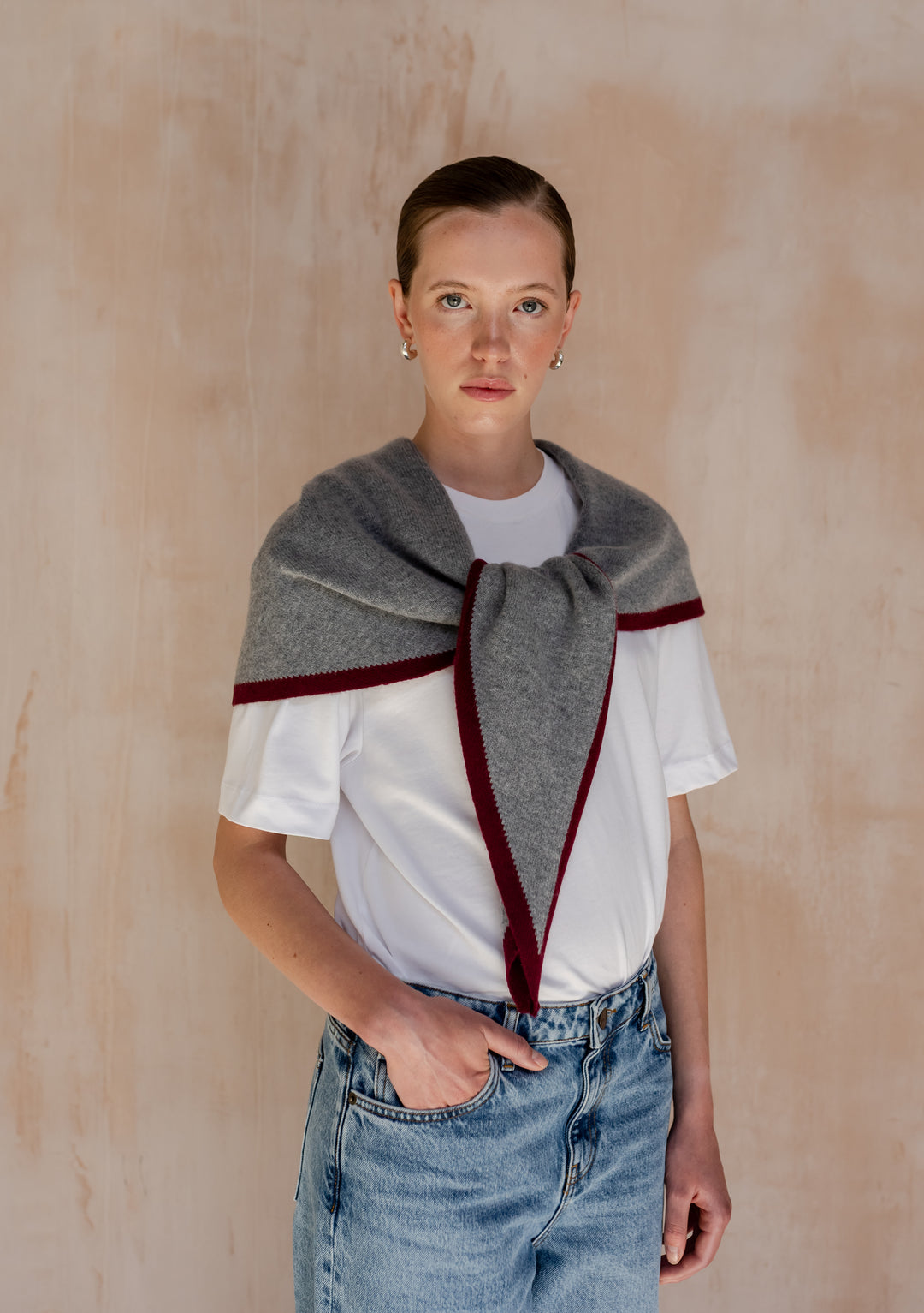 Young person wearing TBCo Large Merino Wool Triangle Scarf in Charcoal & Burgundy over white t-shirt and jeans, showcasing its draped style with burgundy edge detail.