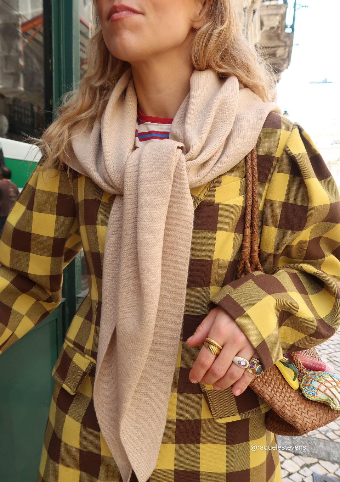 Woman in checkered jacket, with a beige sweater and chunky rings, holding a straw bag. Featured: TBCo Large Merino Wool Triangle Scarf in Oatmeal.