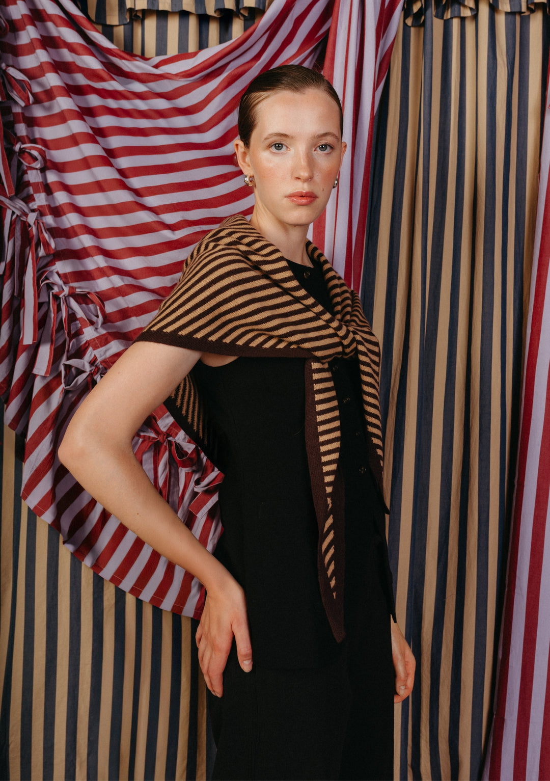 Young woman models TBCo Large Merino Wool Triangle Scarf in camel and brown stripe, draped over shoulders, highlighting its versatile styling and soft merino wool texture.