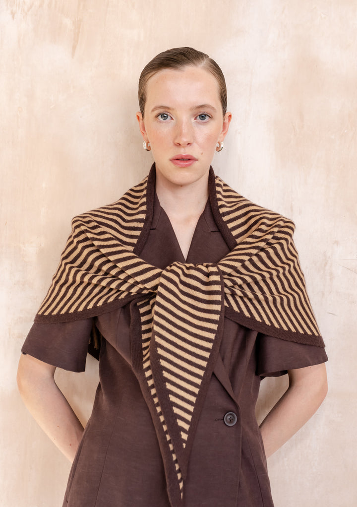 Young woman models the TBCo Large Merino Wool Triangle Scarf in Camel & Brown Stripe, draped over a dark brown buttoned garment.