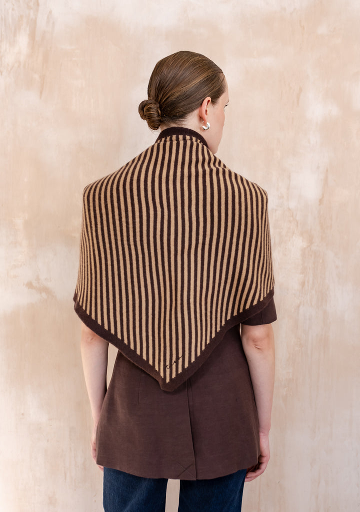 Person wearing TBCo Large Merino Wool Triangle Scarf in Camel & Brown Stripe, draped over shoulders, showcasing narrow vertical stripes and solid brown edges, styled with chocolate-brown top.