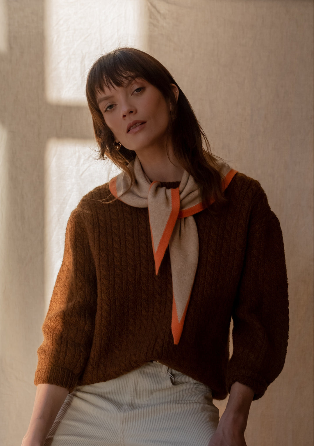 TBCo Merino Triangle Scarf in camel with apricot trim styled with brown cable knit jumper in warm, natural lighting