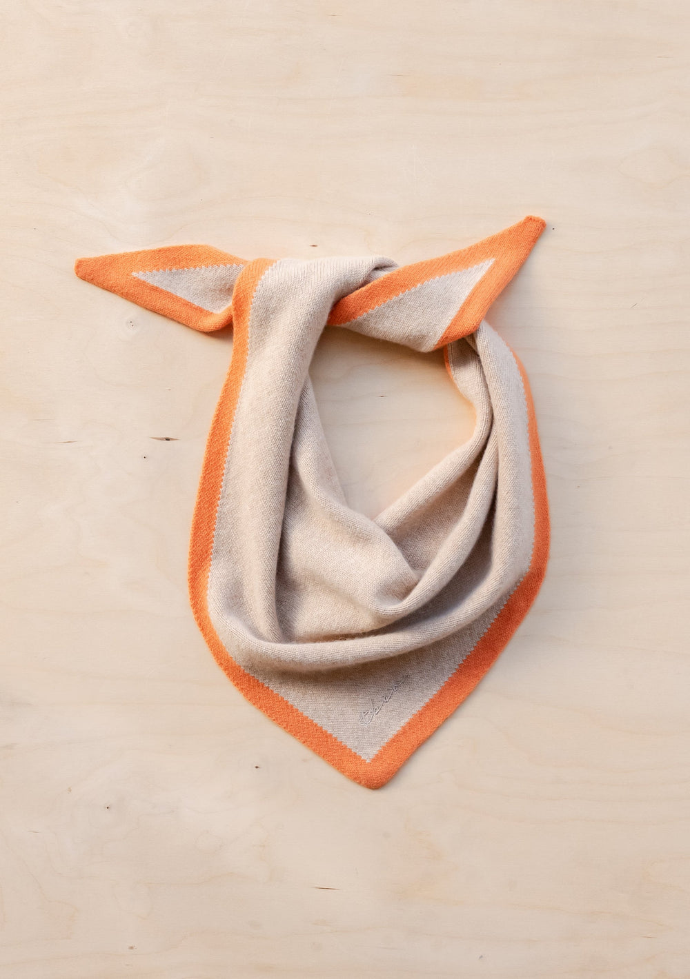 TBCo Merino Triangle Scarf in camel with apricot border, styled in an elegant knot on beige background