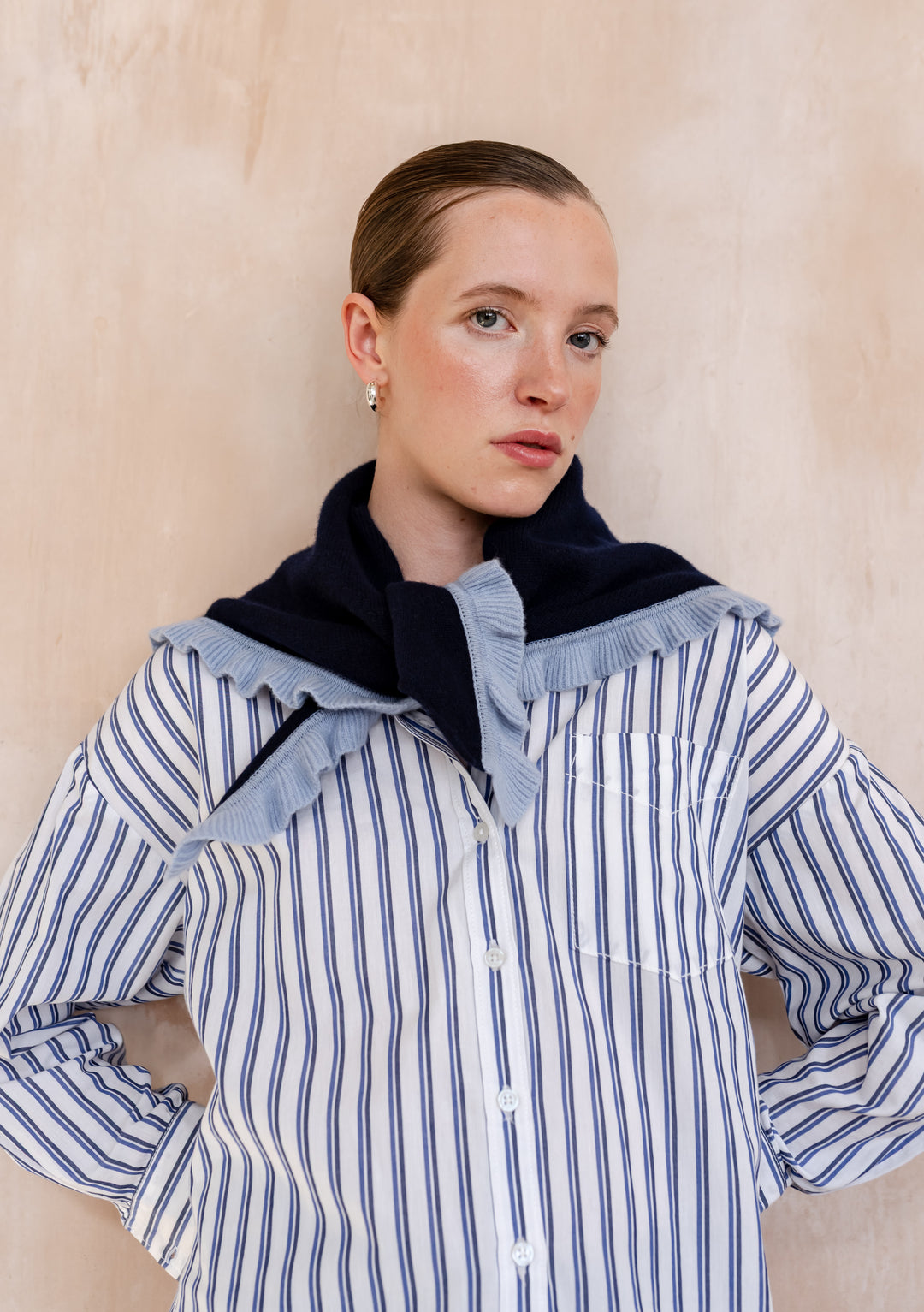 Woman models TBCo Merino Wool Triangle Scarf in Navy Ruffle, draped over shoulders, showcasing its light-blue ruffle trim and soft merino wool texture.