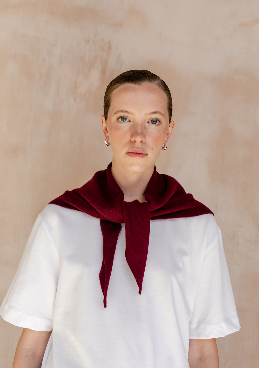 Young person wearing a plain white T-shirt with a TBCo Merino Wool Triangle Scarf in Burgundy draped over shoulders, showcasing its versatile styling and elegance.