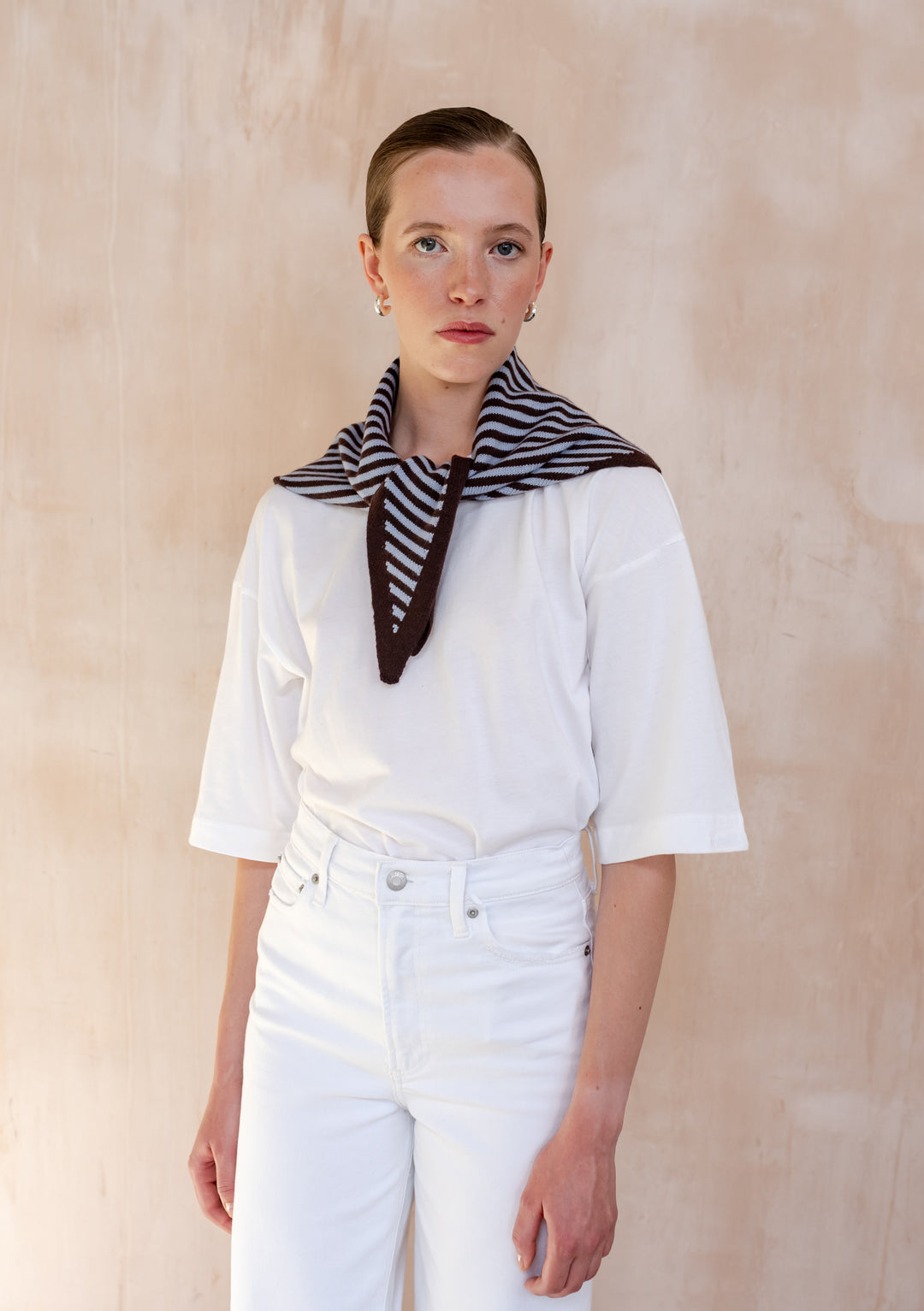 Person wearing a TBCo Merino Wool Triangle Scarf in Blue & Brown Stripe, draped over a white tee and jeans, showcasing minimalist style.