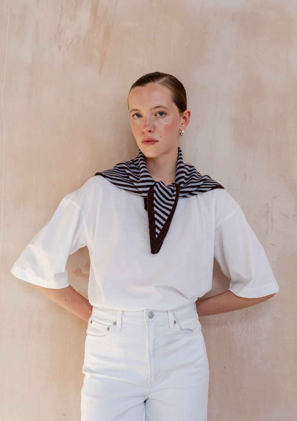 Woman wearing TBCo Merino Wool Triangle Scarf in Blue & Brown Stripe, draped over white outfit, showcasing its lightweight design and versatile tie options.