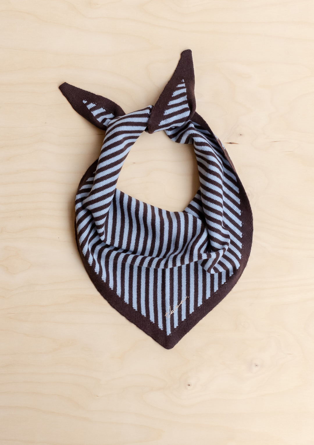 TBCo Merino Wool Triangle Scarf in Blue & Brown Stripe, laid flat with tied corners, showcasing its alternating stripe pattern on a light wood surface.