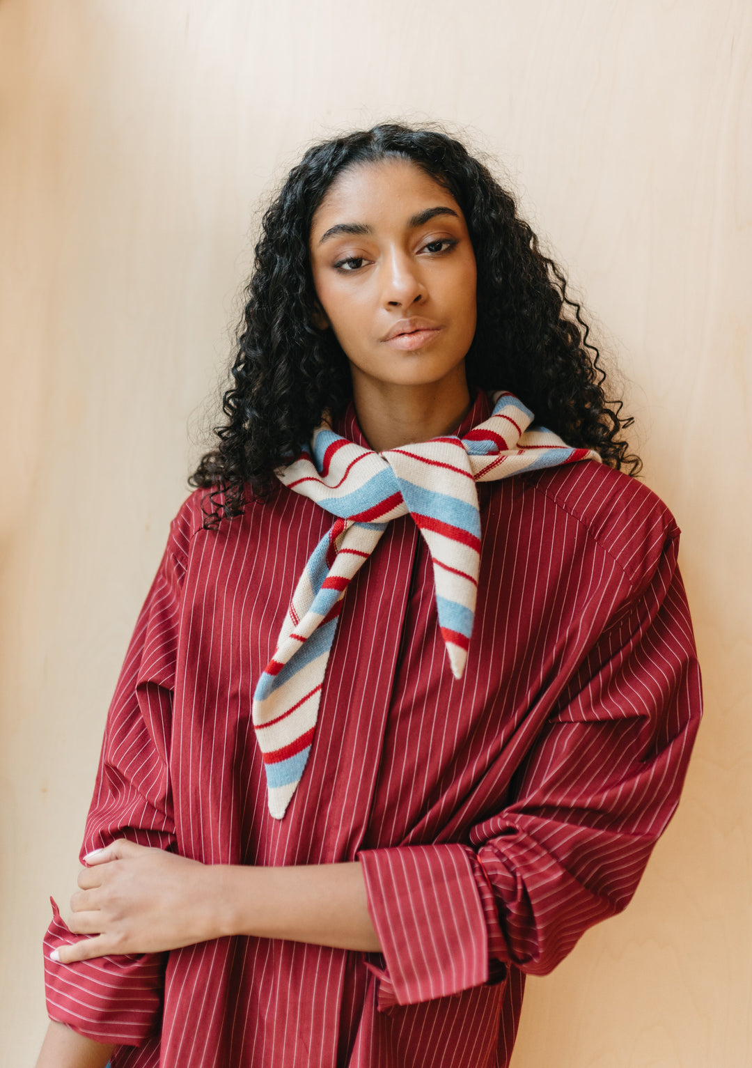 Model wearing TBCo Merino Wool Triangle Scarf in Blue & Red Stripe, tied loosely over red pinstripe shirt