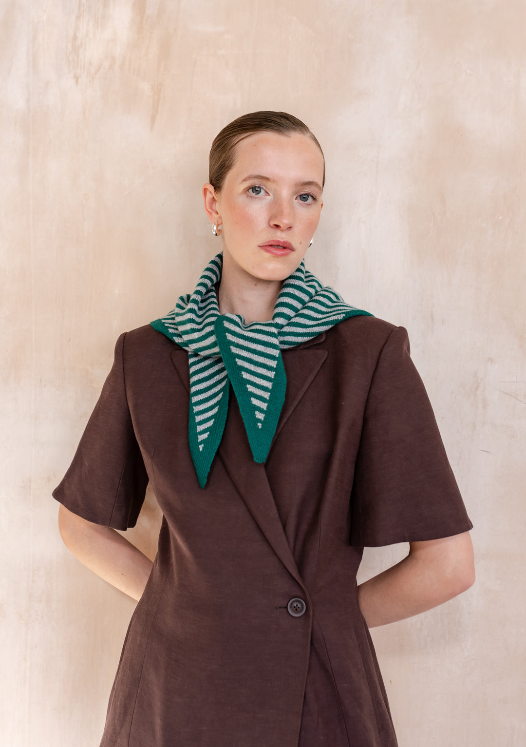 Person wearing a dark brown blazer and showcasing the TBCo Merino Wool Triangle Scarf in Green & Charcoal Stripe, highlighting its soft texture and versatile styling.