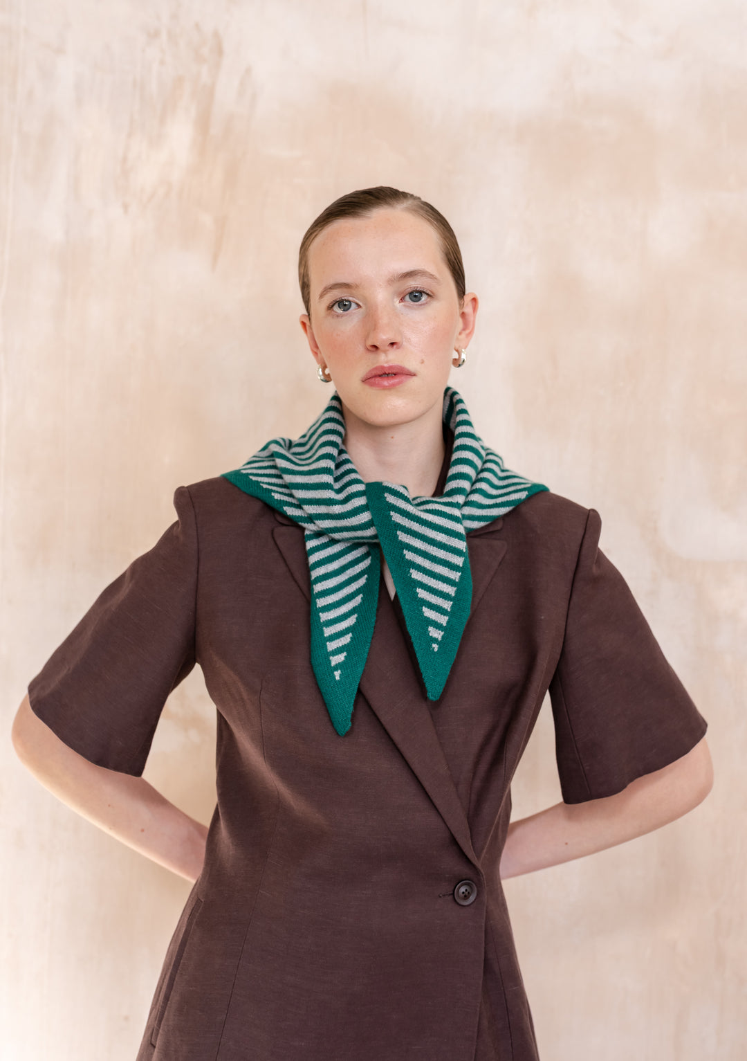 Young person wearing TBCo Merino Wool Triangle Scarf in Green & Charcoal Stripe over chocolate-brown blazer, showcasing its versatile design and elegant drape.