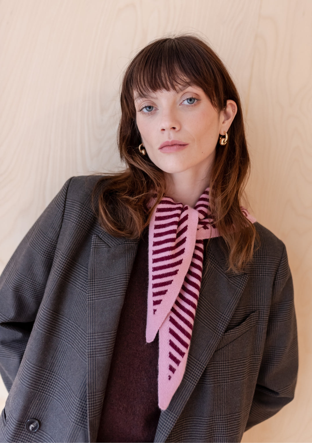 Pink and burgundy striped merino triangle scarf by TBCo styled with grey plaid blazer and burgundy jumper against beige backdrop