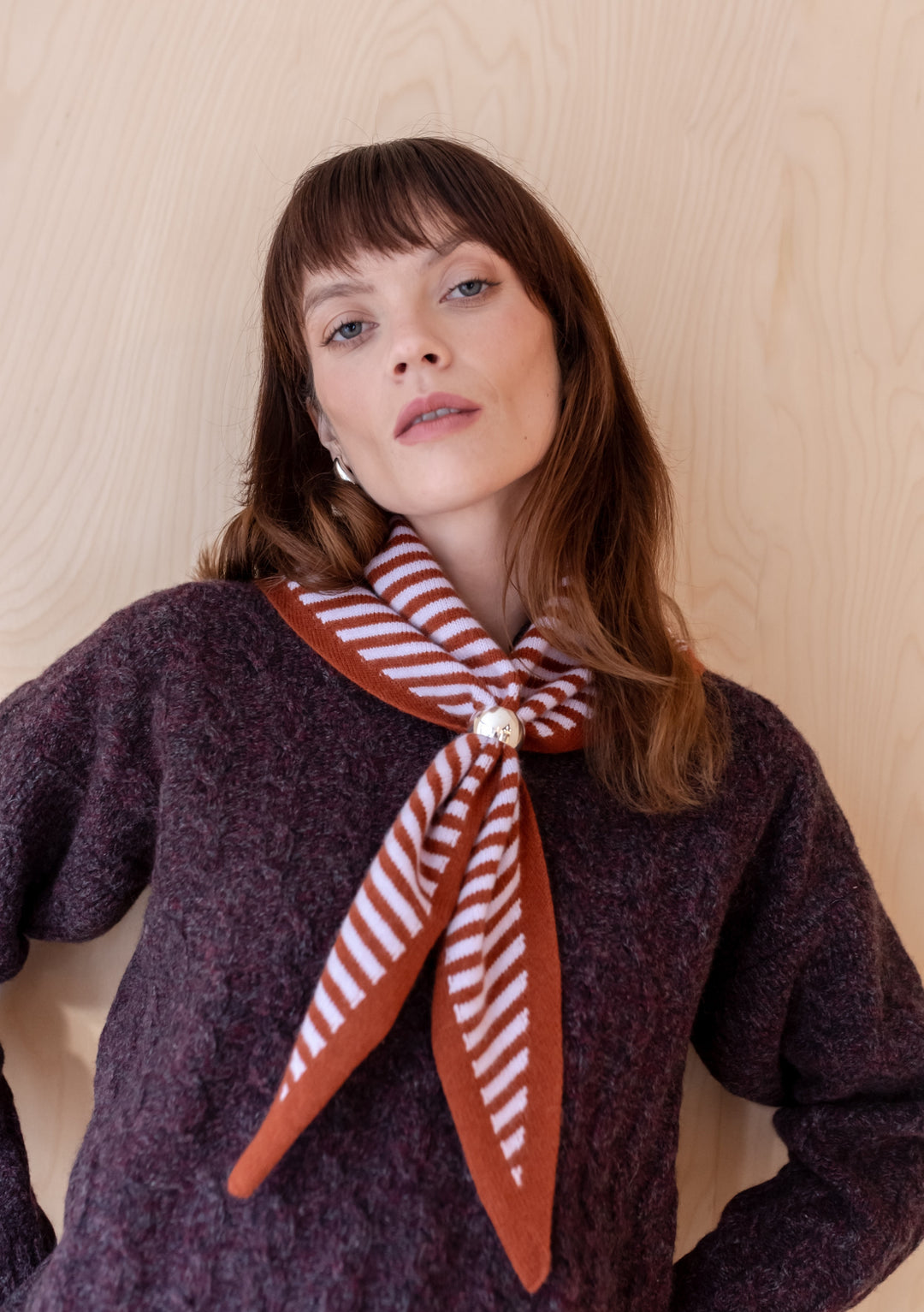 TBCo Merino Triangle Scarf in lilac and rust stripes styled with purple jumper, showcasing elegant drape and embroidered logo detail