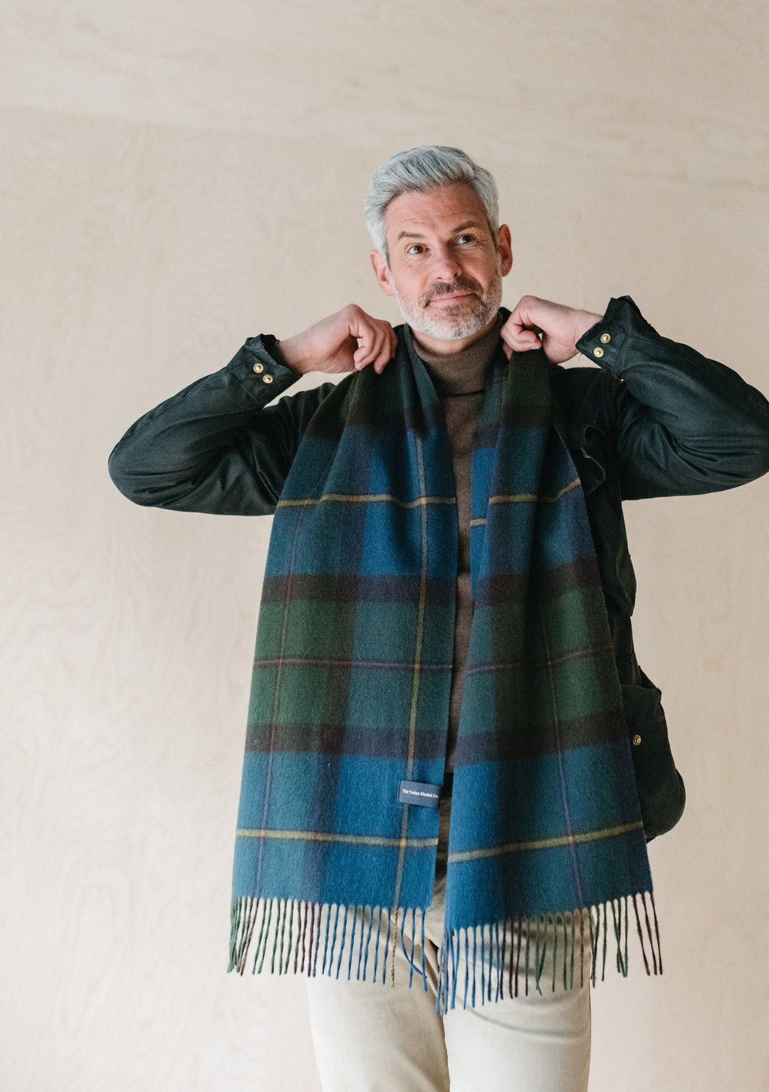 TBCo Macleod of Harris Antique Tartan lambswool scarf styled with black jacket and cream trousers against neutral backdrop