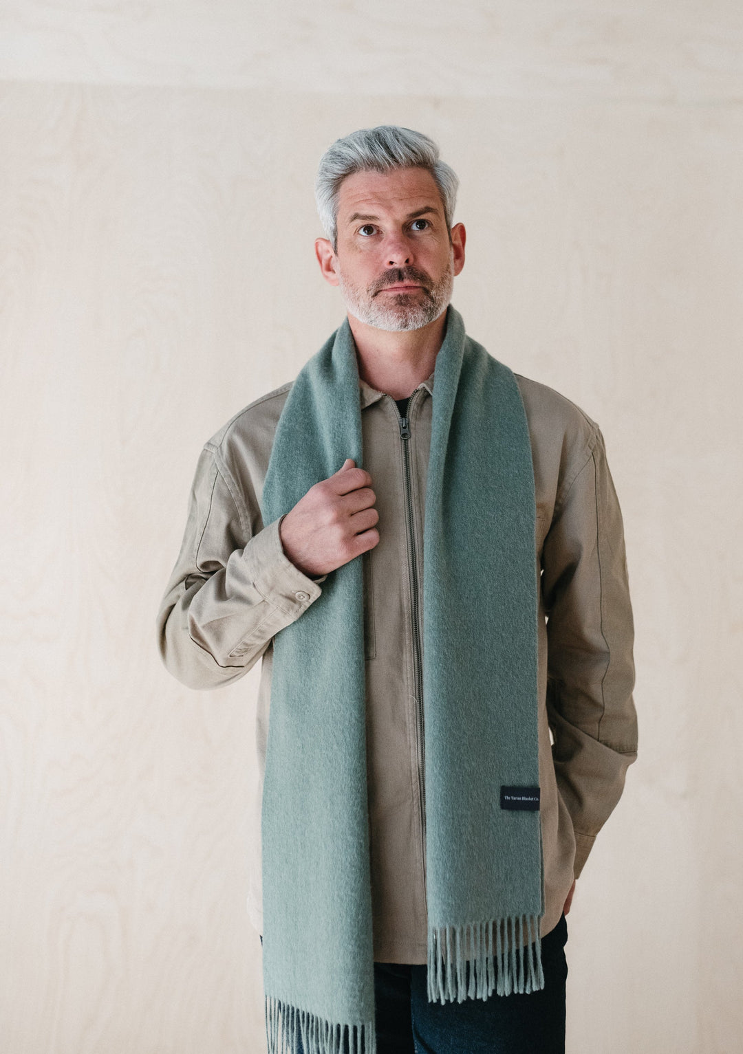 TBCo Men's Lambswool Scarf in Sage Melange styled with beige jacket, showcasing soft texture and elegant fringed design