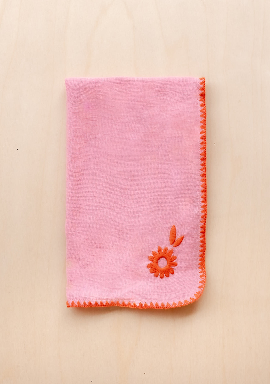 TBCo Cotton & Linen Napkin in pink with orange floral embroidery and decorative edge stitching displayed on beige surface