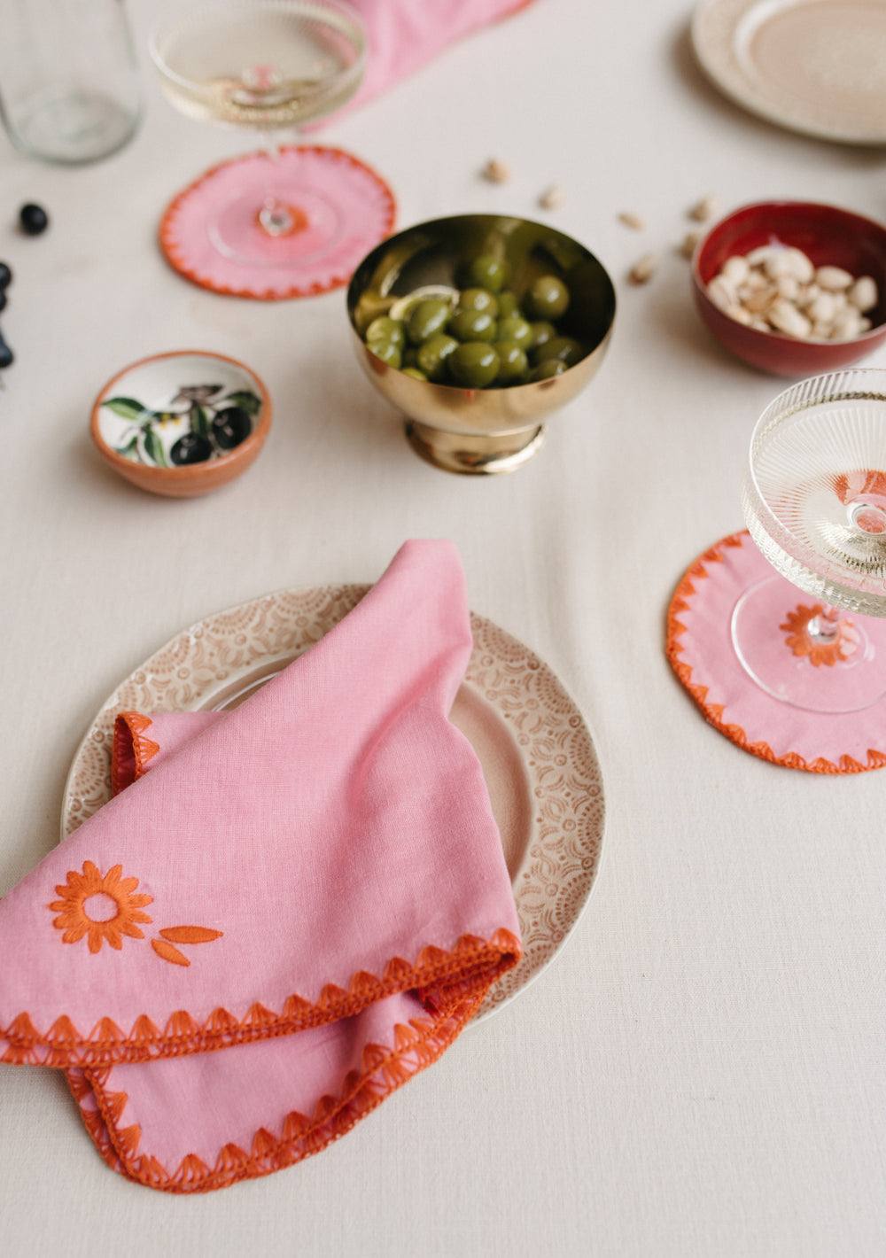 Pink TBCo Cotton & Linen Napkins with orange floral embroidery set on table with olives and coasters for elegant dining