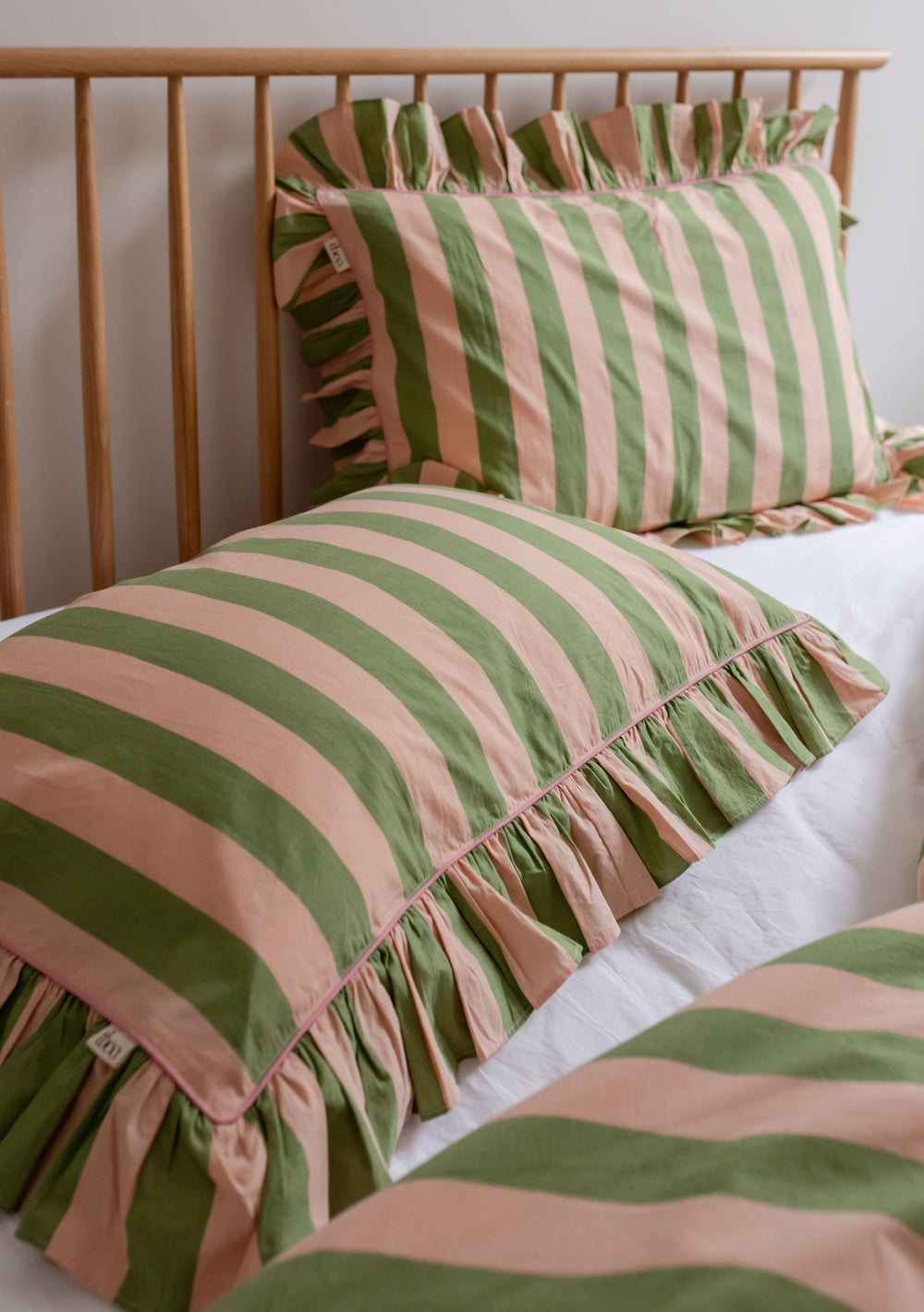 TBCo cotton pillowcases with green and white stripes and delicate ruffled edges, displayed on wooden bed frame