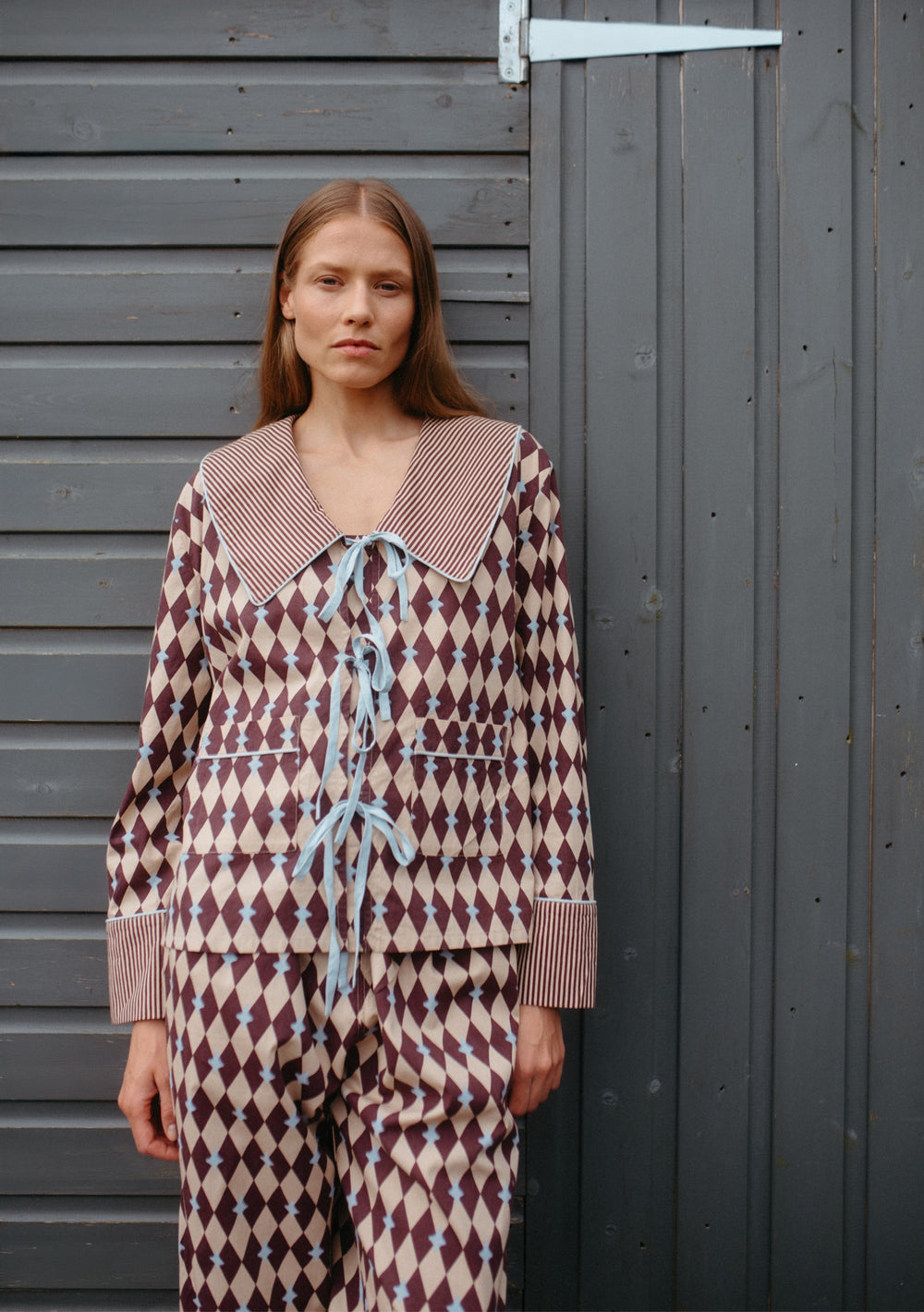 Woman wearing TBCo Cotton Pyjamas in Camel Harlequin with blue bow ties, striped collar, and elastic waistband.