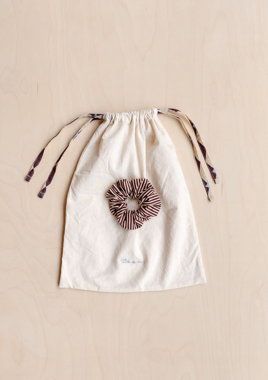 Cotton Pyjamas in Camel Harlequin by TBCo storage bag and matching striped scrunchie on wooden background.