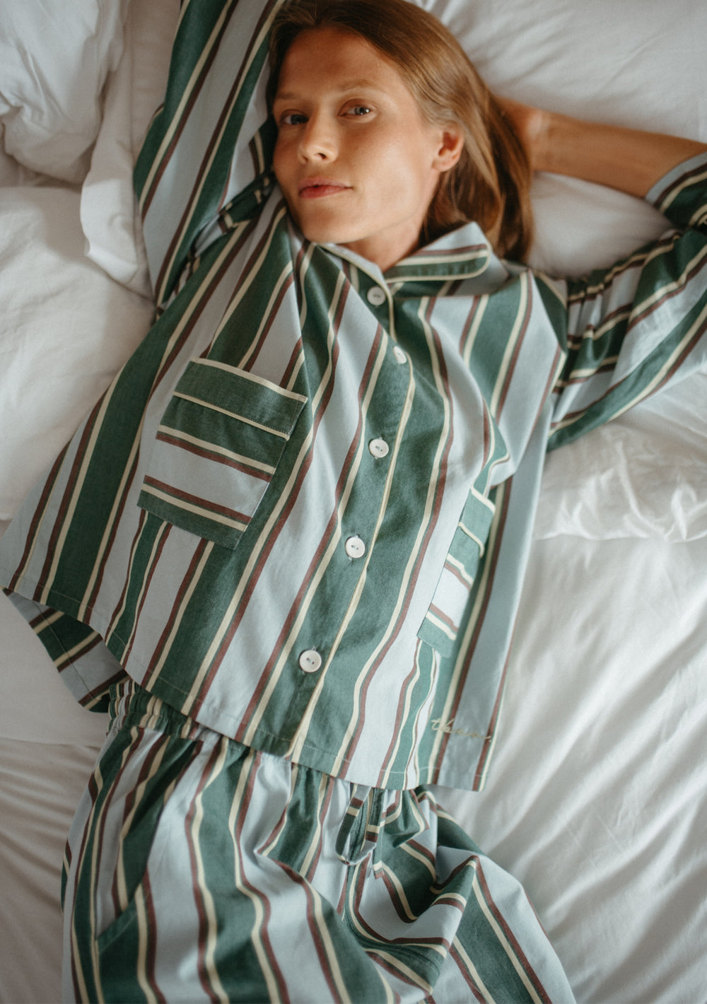 Woman wearing TBCo Cotton Pyjamas in Blue Stripe lying on bed, showcasing breathable, striped cotton poplin set.