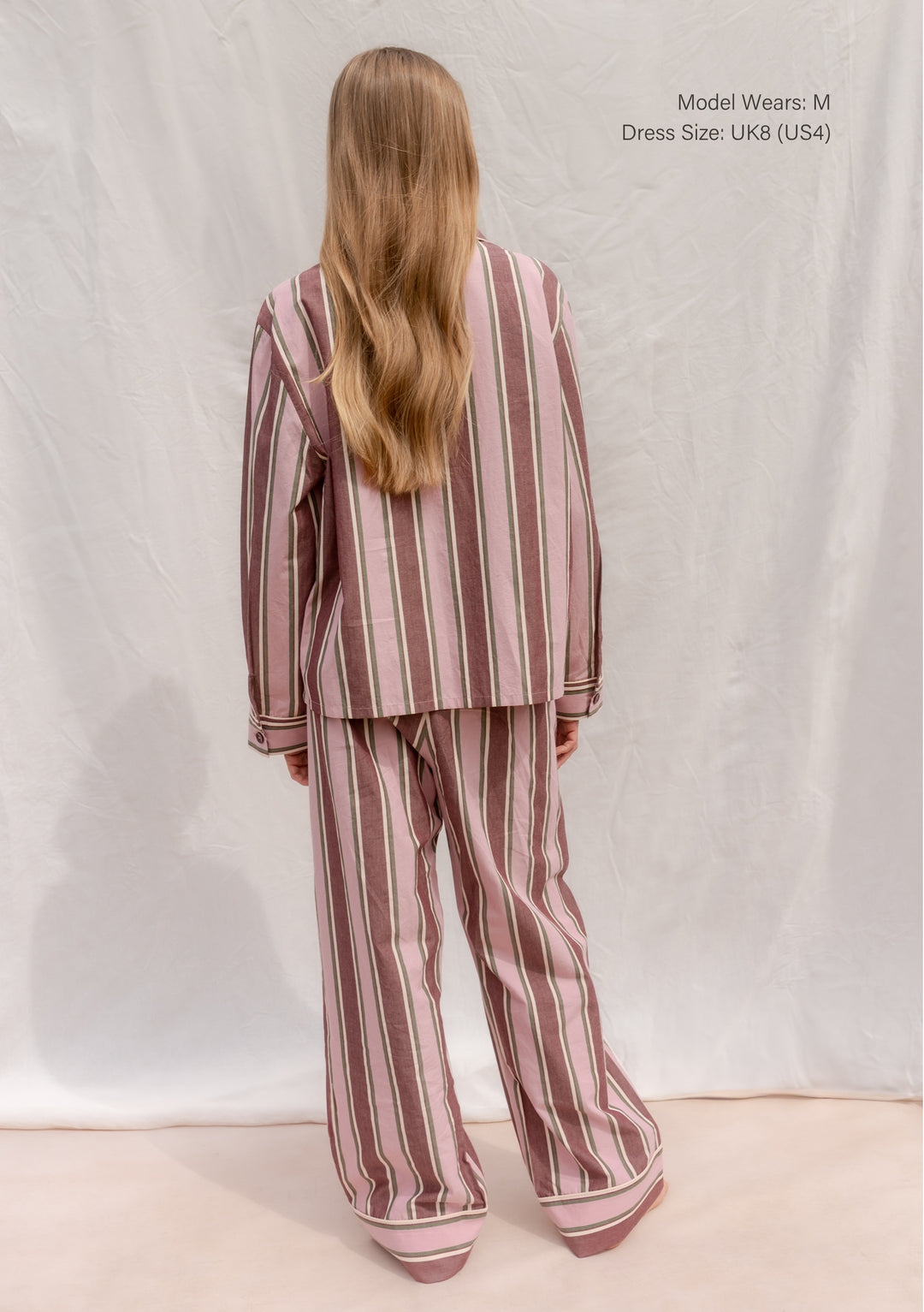 Back view of TBCo Cotton Pyjamas in Pink Stripe worn by model with long hair in a relaxed pose.