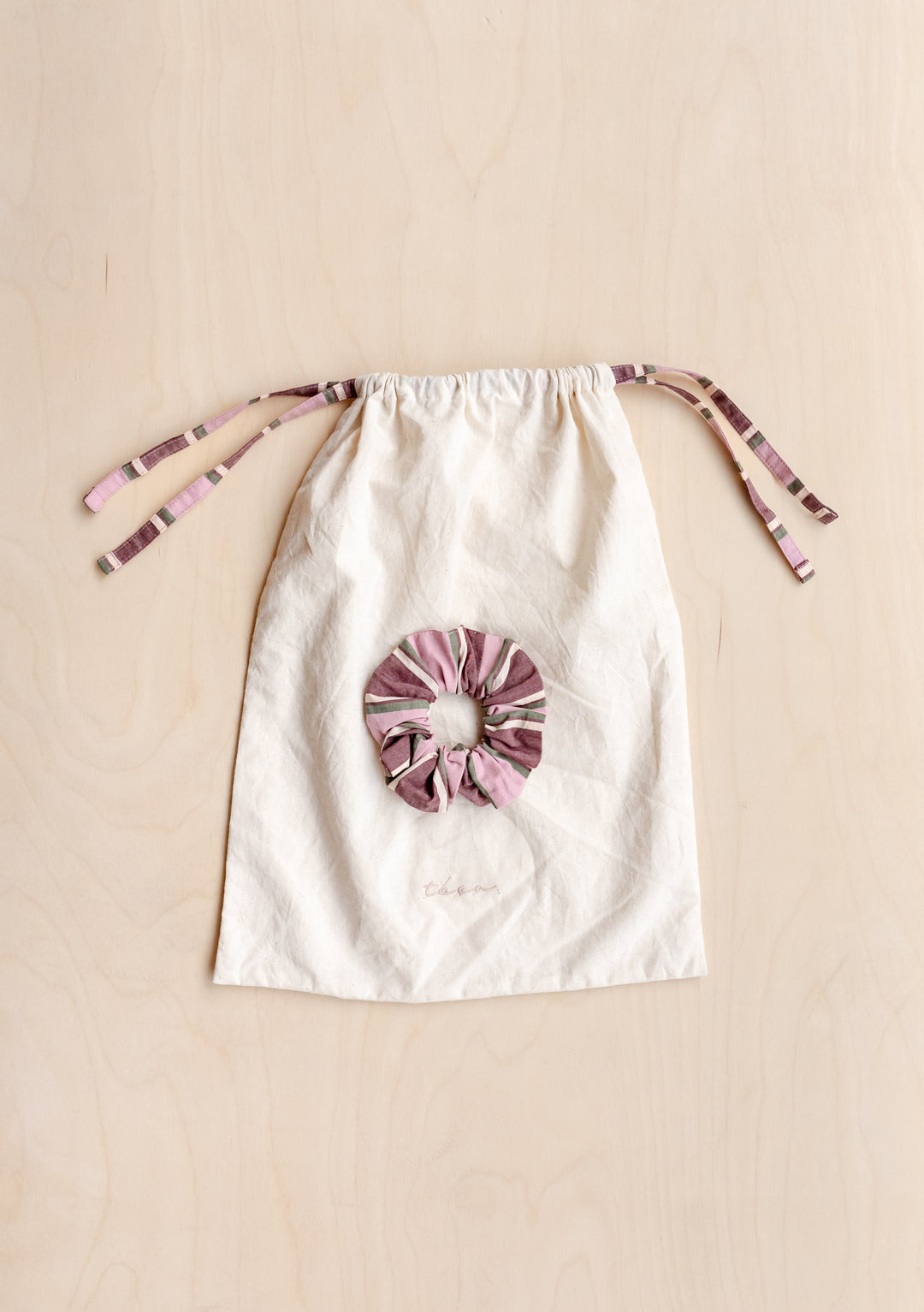 Cotton Pyjamas in Pink Stripe by TBCo drawstring bag with matching pink striped scrunchie on wooden surface
