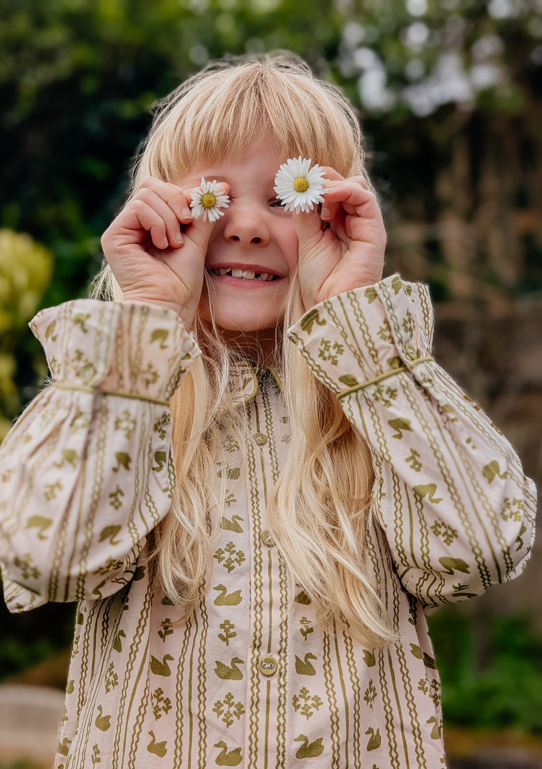 Child holding flowers over eyes wearing TBCo Cotton Kids Pyjamas in Olive Swan with patterned soft cotton fabric
