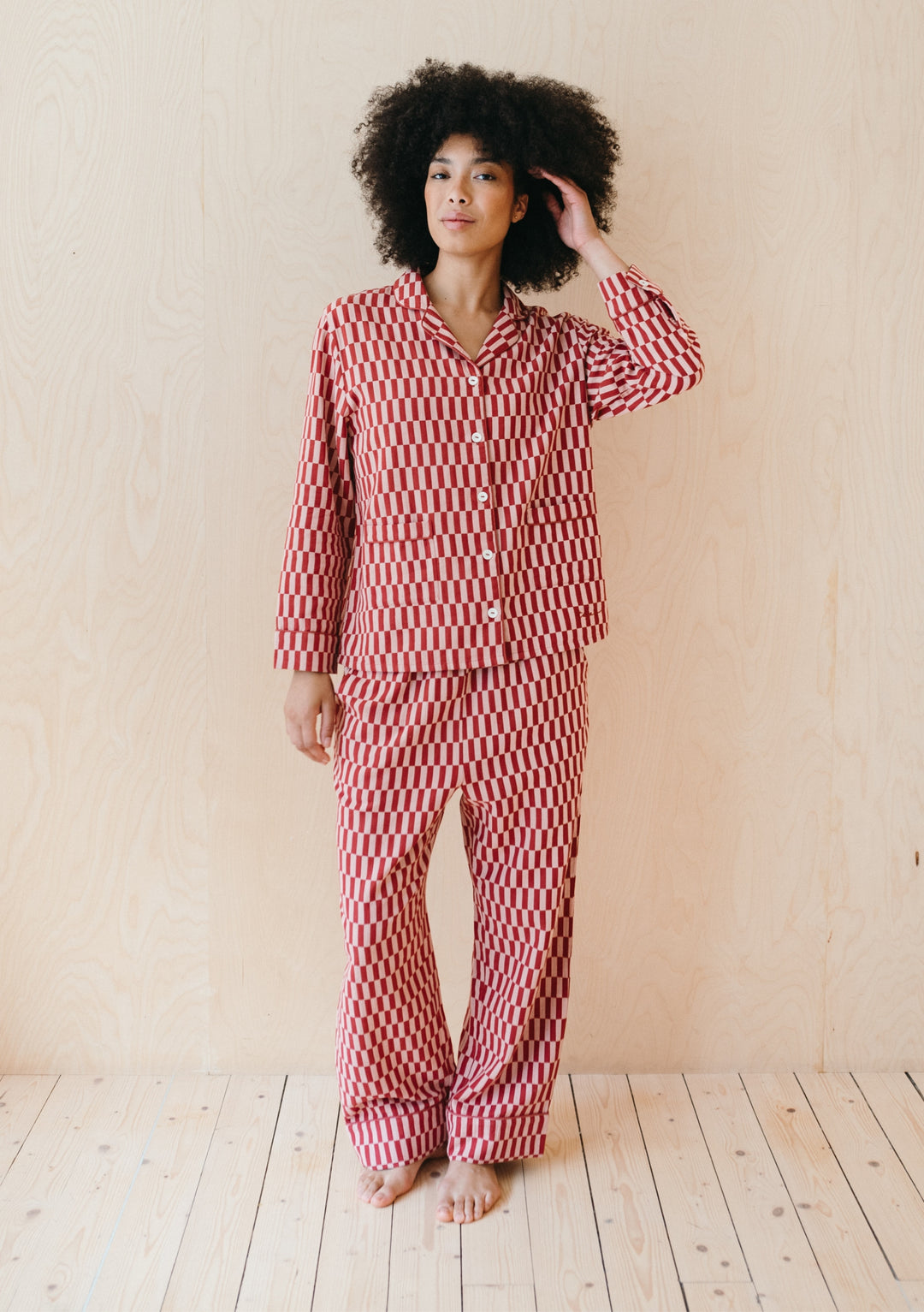 Model wearing TBCo Cotton Pyjamas in Rose Checkerboard pattern, featuring long-sleeve button-up top and matching trousers against neutral wall