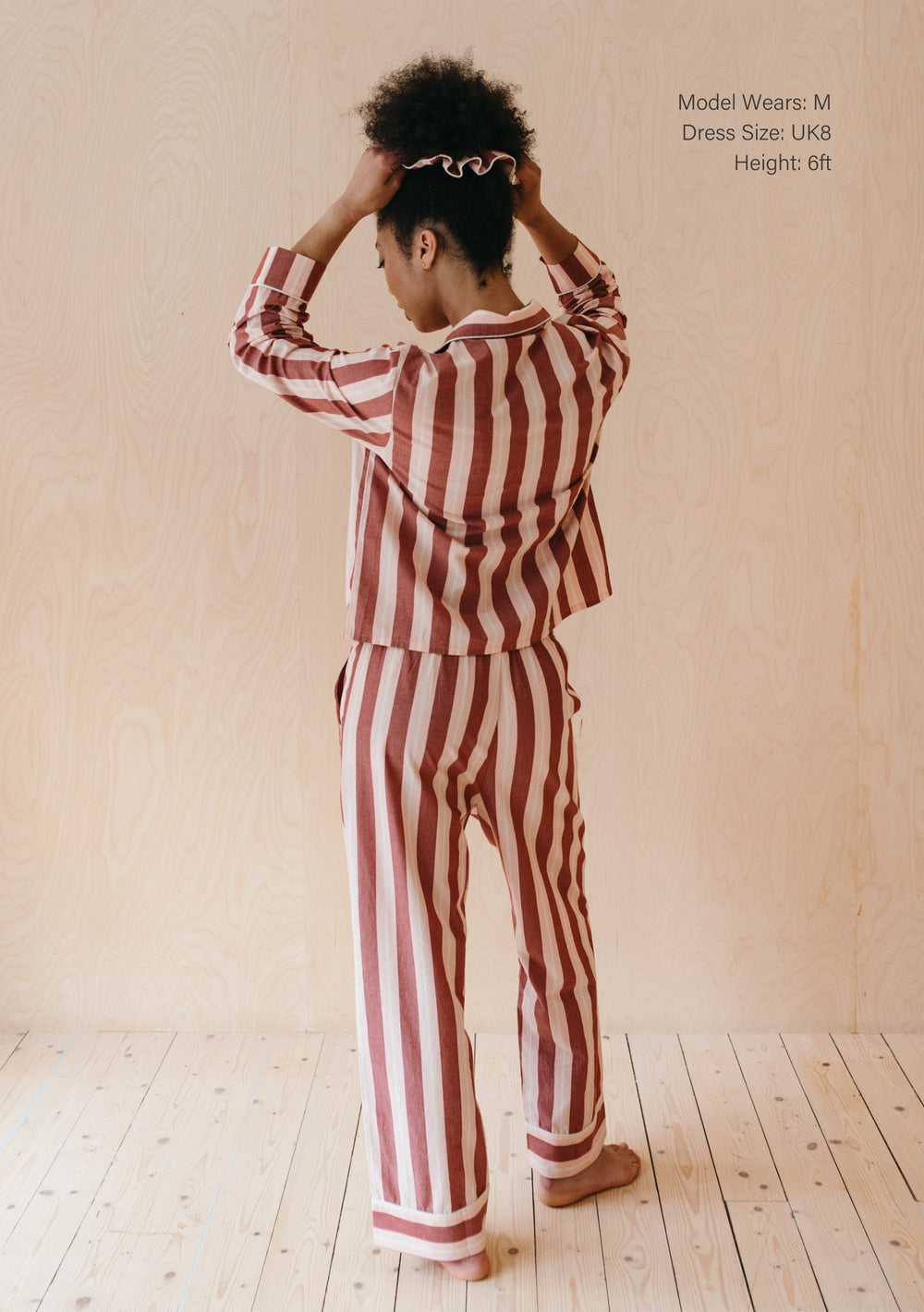 Back view of TBCo Cotton Pyjamas in Red Stripe, showing vertical striped pattern and relaxed fit design on wooden floor