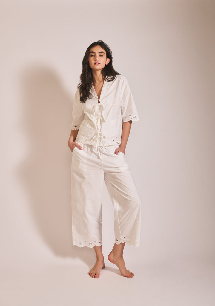 Woman wearing TBCo Cropped Cotton Pyjamas in White Shell with scalloped eyelet hem and relaxed cropped trousers standing against plain backdrop