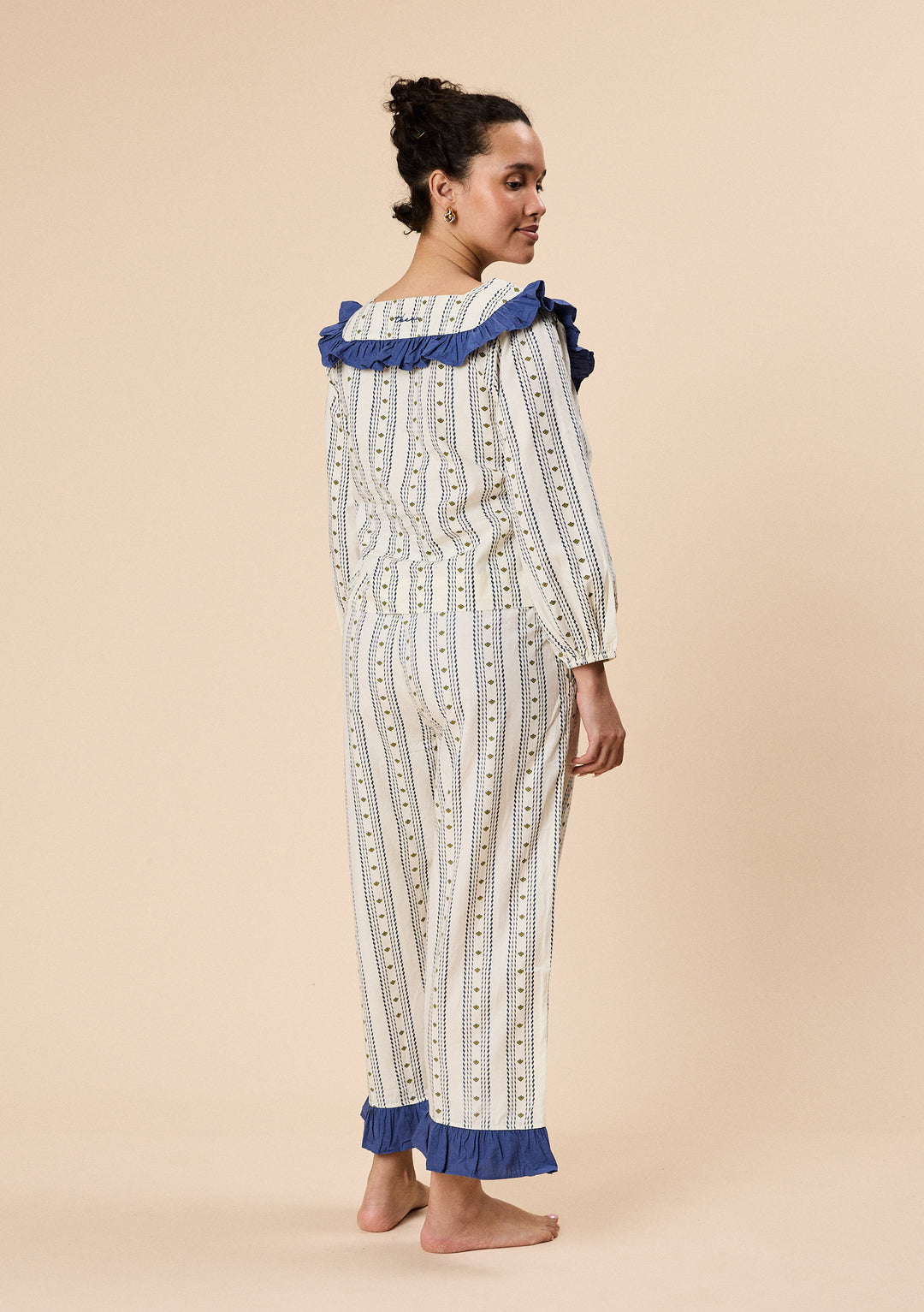 Model wearing TBCo Cropped Cotton Pyjamas in Navy Ditsy Floral with blue ruffle trim and loose comfortable fit from the back view