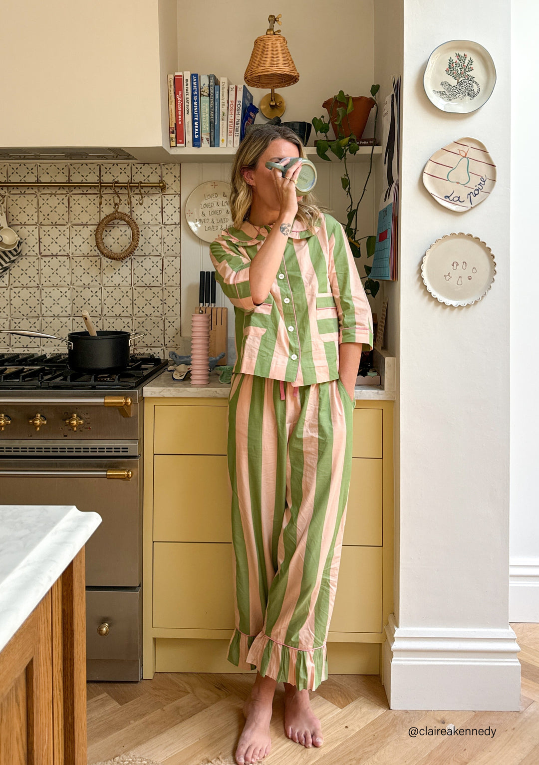 Person wearing TBCo Cotton Pyjamas in Green Stripe with ruffled collar, standing in stylish kitchen with decorative plates