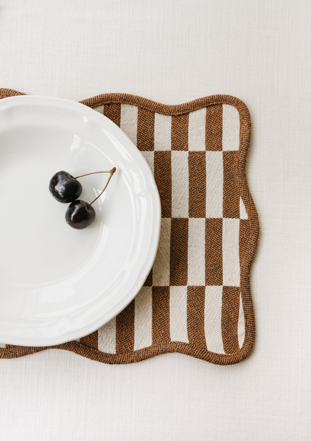 TBCo Cotton Placemats in camel and cream checkerboard pattern with scalloped edges, shown with white plate and cherries