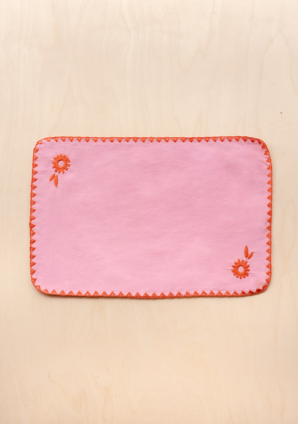 Pink cotton and linen TBCo placemat with orange floral embroidery and decorative stitched edges, rectangular table setting