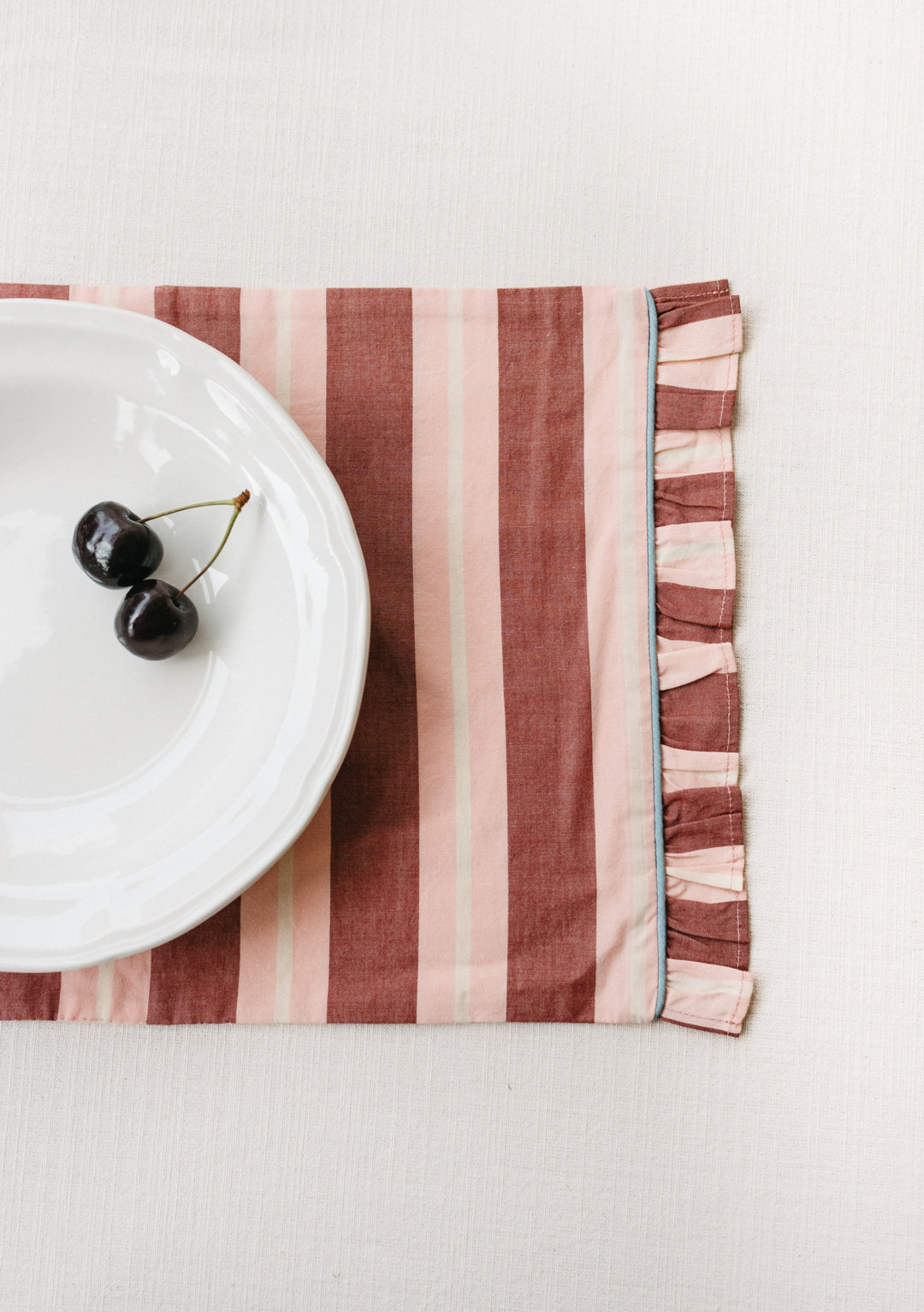 TBCo Cotton Placemats Set of 2 in Red Stripe with frilled edge and blue piping, shown with white plate and cherries