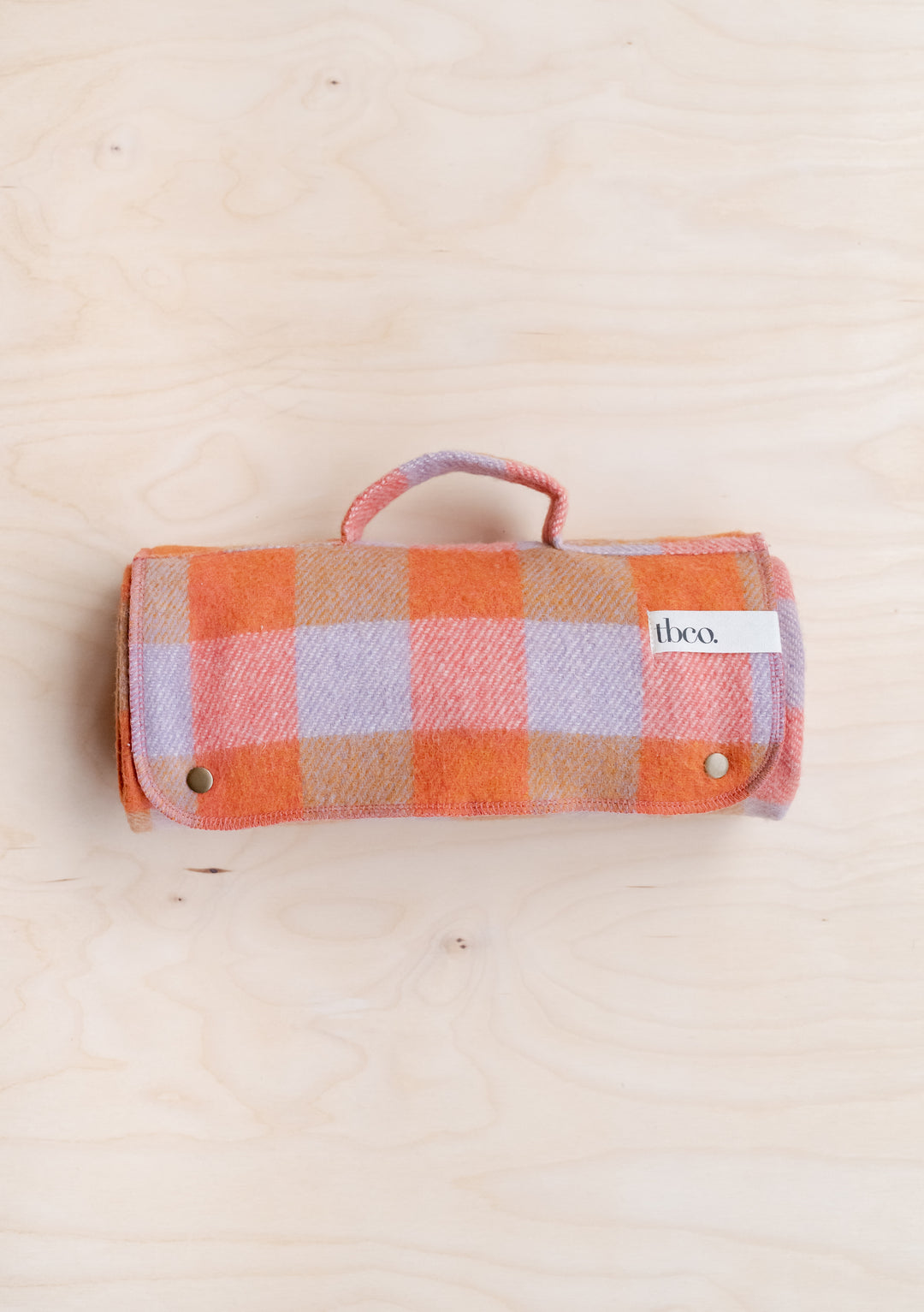 TBCo Recycled Wool Small Picnic Blanket in Orange Gingham, rolled and secured with poppers, displaying lilac and orange check pattern