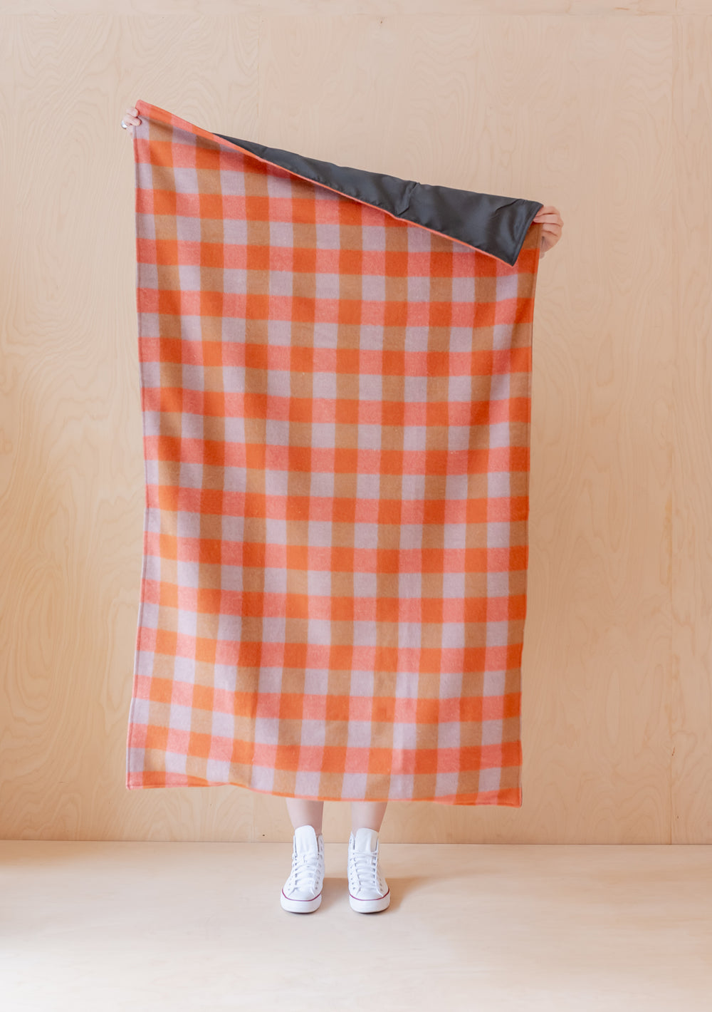 TBCo Recycled Wool Small Picnic Blanket in orange gingham pattern with water resistant backing, displayed unfolded against beige wall