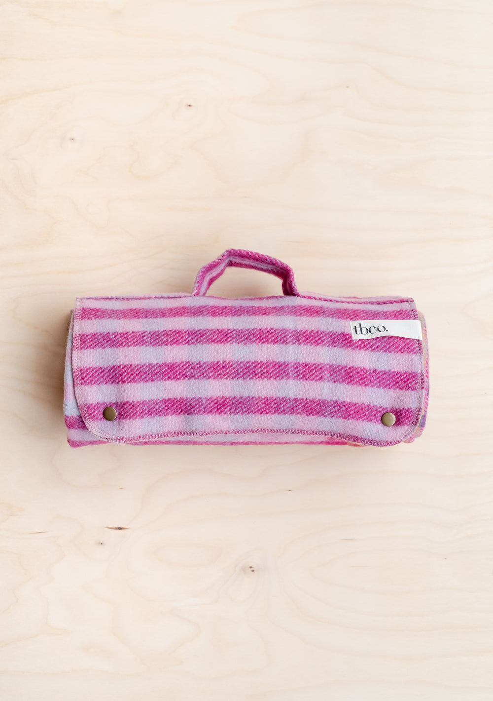 TBCo recycled wool picnic blanket in pink gingham pattern, rolled and secured with poppers, featuring carry handle