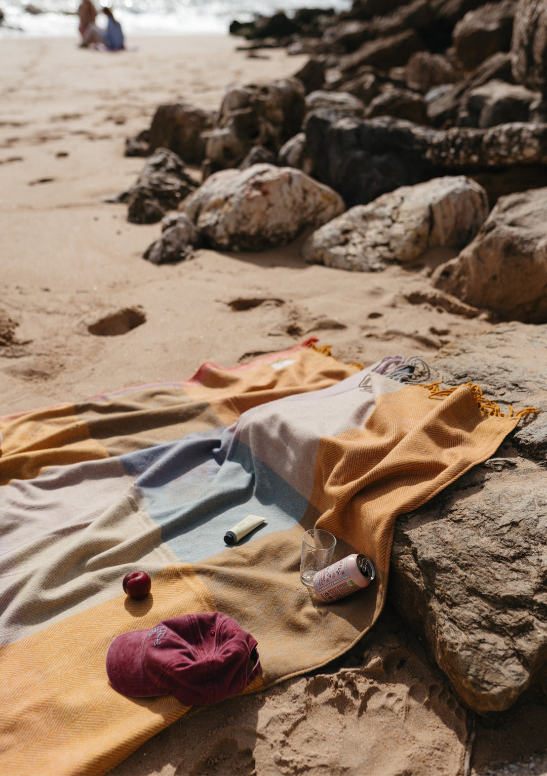 TBCo Recycled Wool Picnic Blanket in Mustard Frame Check laid out on sandy beach with rocks, showing water-resistant backing