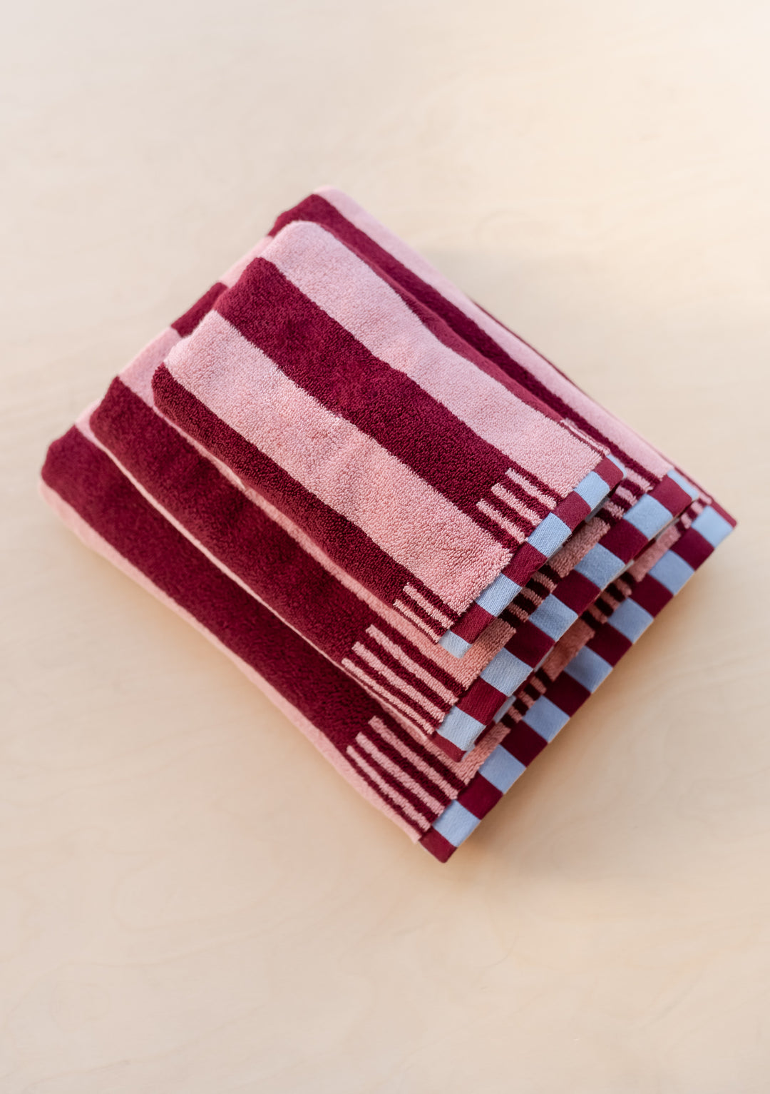 TBCo Cotton Towels in Pink Stripe featuring burgundy stripes and blue checkerboard trim, folded neatly to showcase pattern design